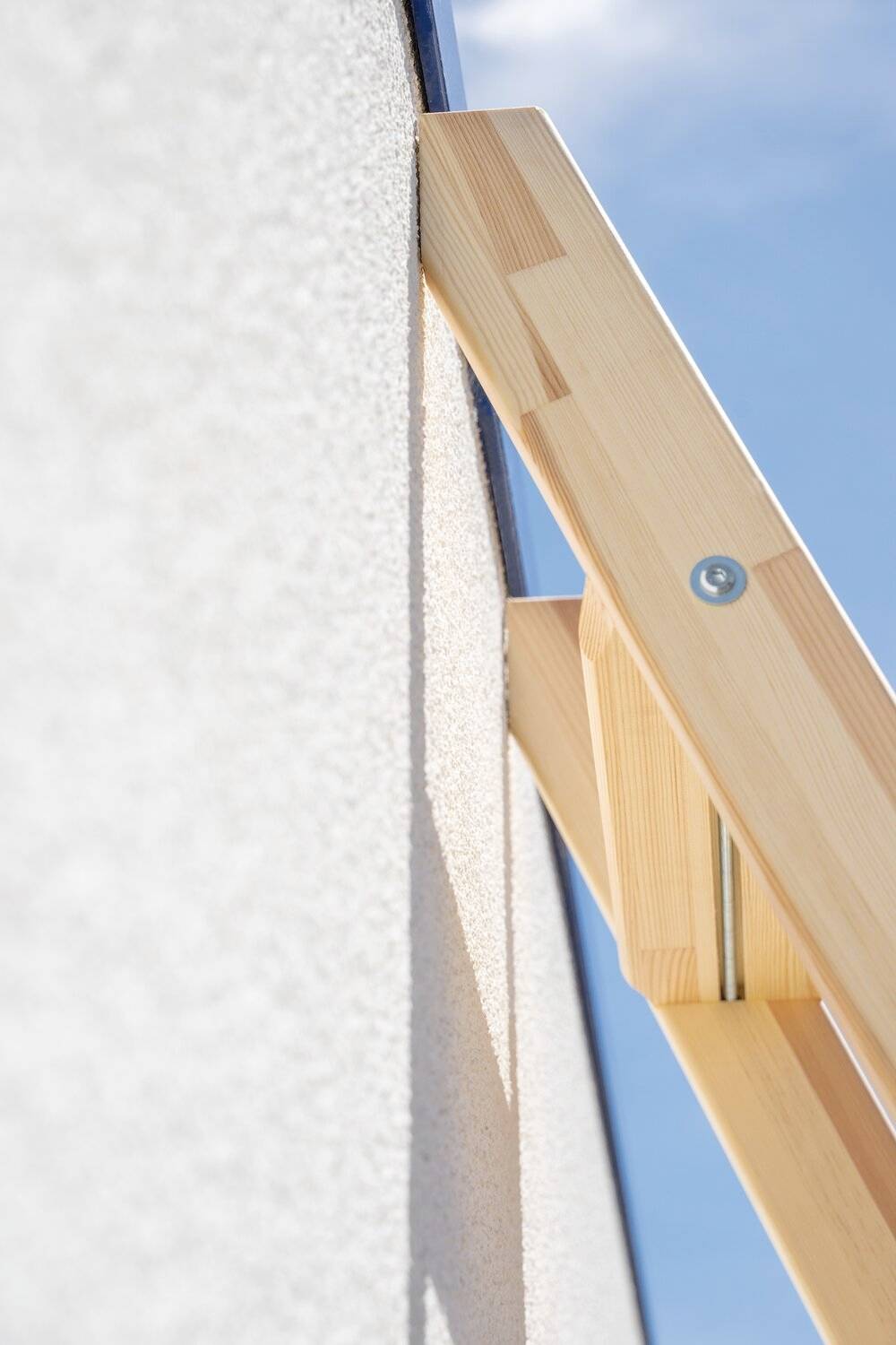 Egy faállvány támaszkodik egy falnak. Egy csavarfej látható. A szög ablaktisztításra vagy -telepítésre utal.