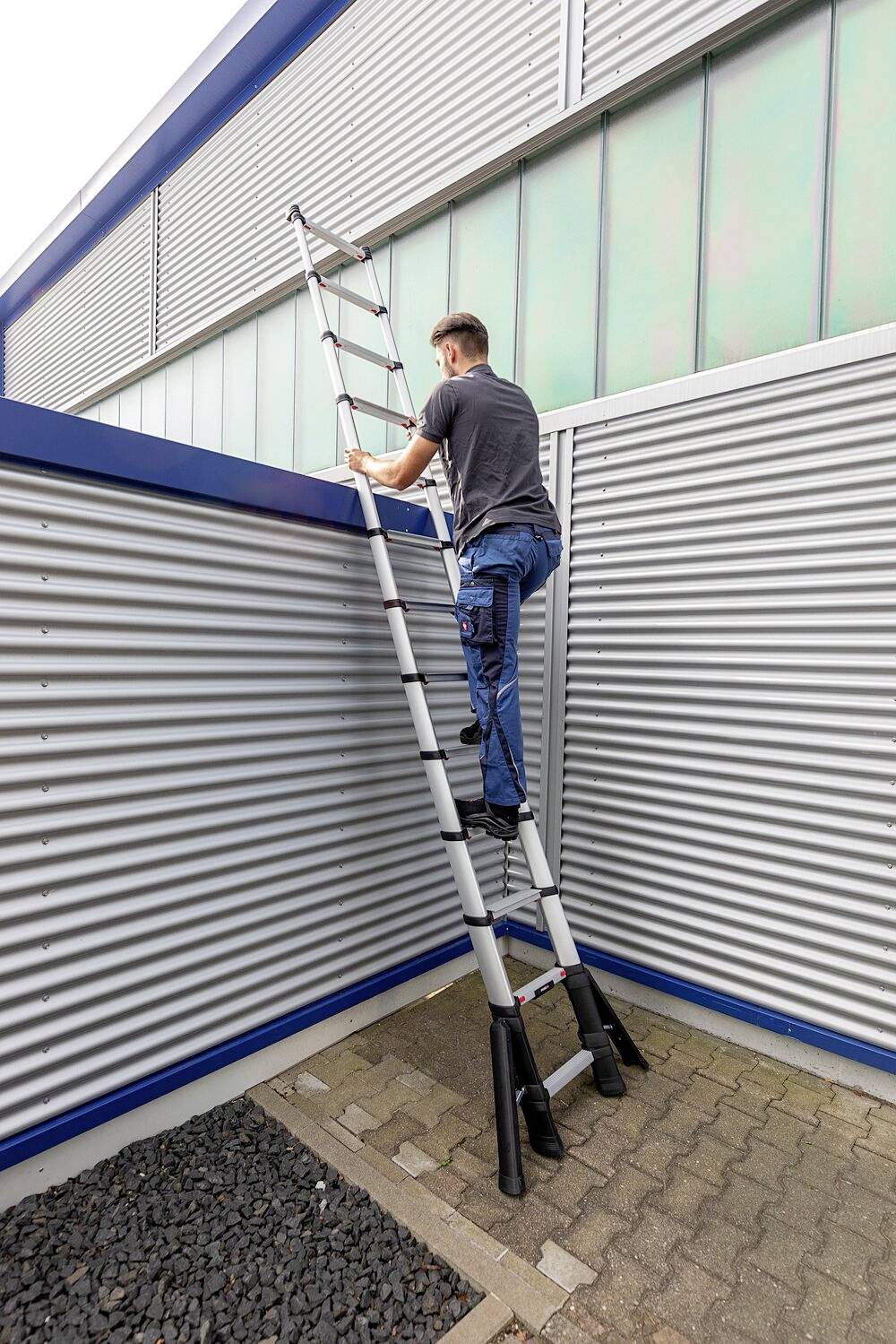 Egy férfi fém épületfalon álló kihúzható létrán mászik fel.