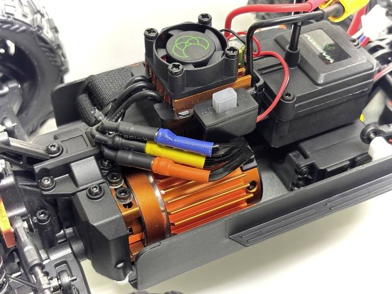 Egy távirányítású autó belső részleteinek közeli felvétele, narancssárga motorral, ventilátorral és különböző színű kábelekkel.