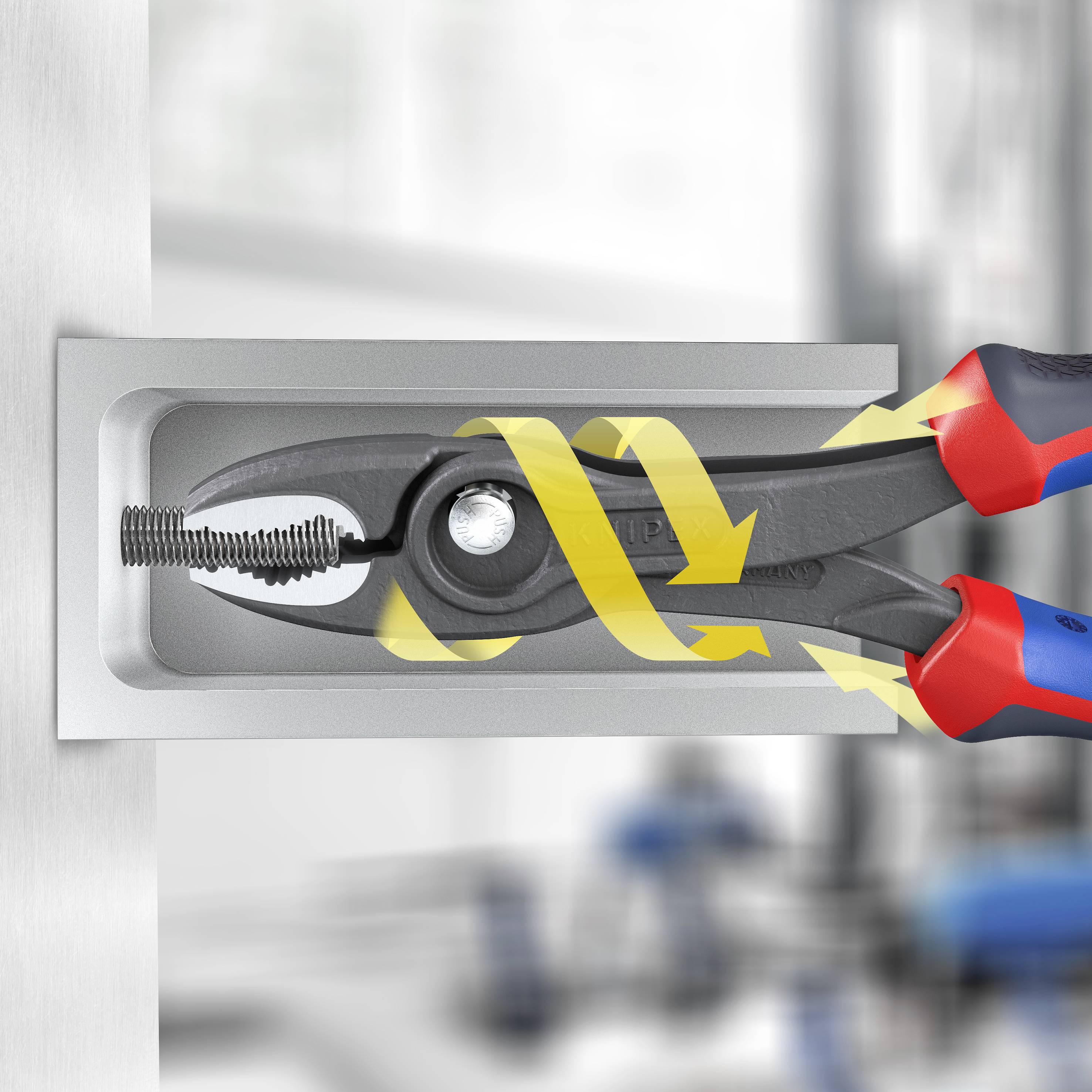 Egy piros-kék dizájnú szerszámfogantyú egy fémfiókban fekszik. A háttérben egy elmosódott műhelybelső látható.