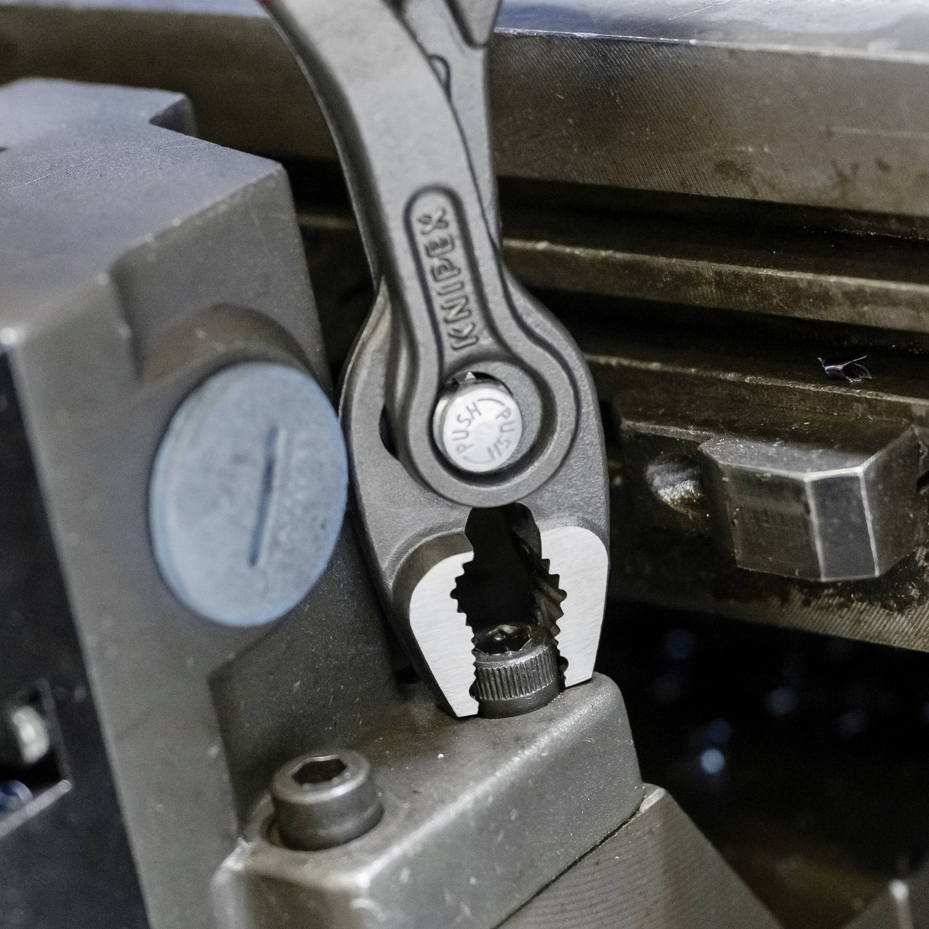 Egy fogó egy fémdarabot fog meg egy műhelykörnyezetben. Szorításban van és munkálják vagy beállítják.