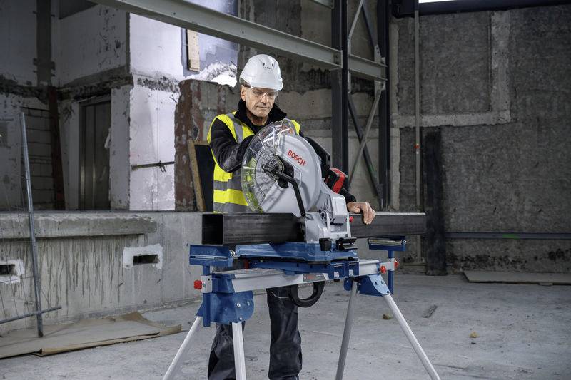 Egy védősisakot és fényvisszaverő mellényt viselő munkás egy fémcsövet vág körfűrésszel egy befejezetlen betonépítményen.