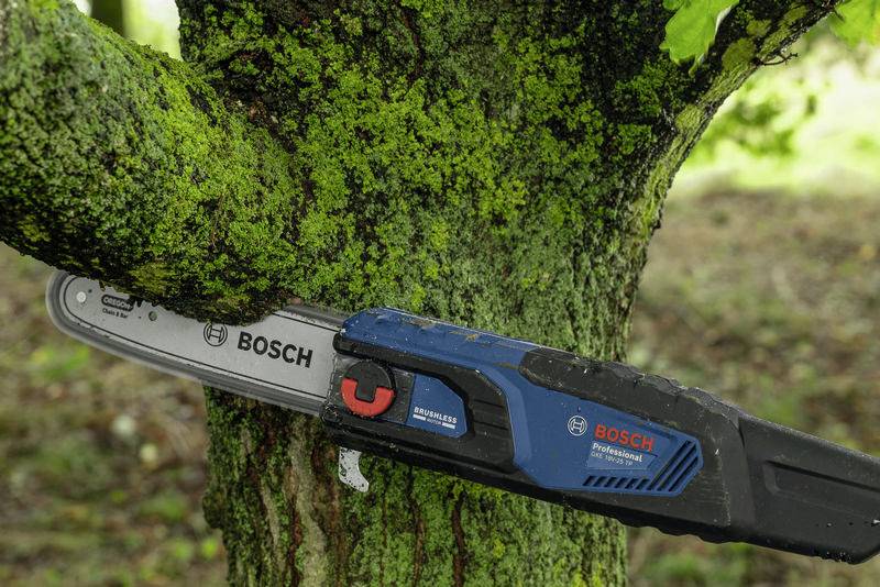 Egy Bosch-láncfűrész egy mohás fáról vág le egy ágat. A szerszám kék-fekete dizájnnal és piros logóval rendelkezik.