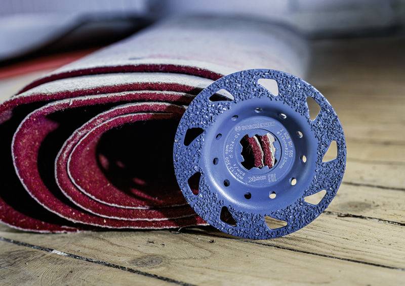 Felgöngyölt vörös szőnyeg fa padlón egy kerek, kék csiszolóeszköz mellett.