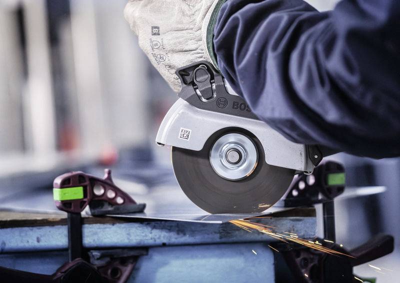 Egy személy elektromos fűrésszel fém anyagot vág, szikrák szóródnak. Munkakesztyűt visel, fémbilincsek rögzítik a munkadarabot.