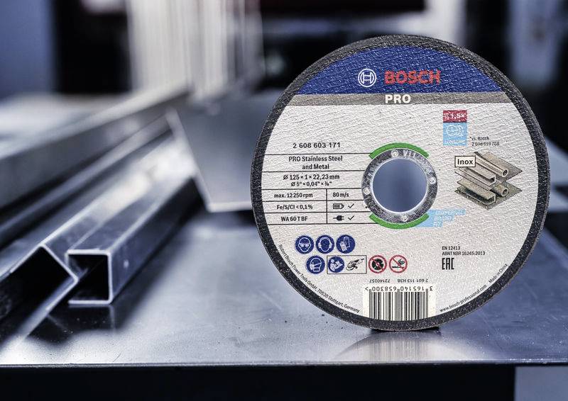 Bosch csiszolótárcsa rozsdamentes acél- és fémkompatibilitással, méretjelöléssel és biztonsági jelzésekkel. A háttérben fémprofilok láthatók.