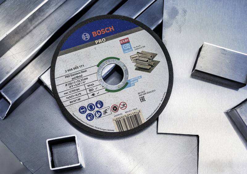 Bosch Pro csiszolókorong fémdarabokon fekszik. A címke specifikációkat mutat: átmérő, anyagtípus és biztonsági szimbólumok.