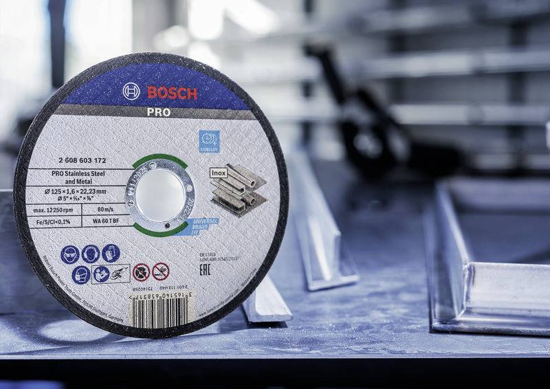 Egy BOSCH PRO és 'Inox' feliratú csiszolótárcsa fekszik az asztalon fémprofil darabok mellett egy műhelyszerű környezetben.
