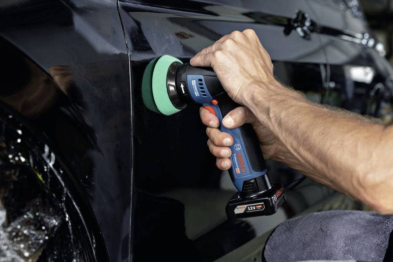 Egy személy egy elektromos polírozógéppel egy fekete autót polírozgat a garázsban.