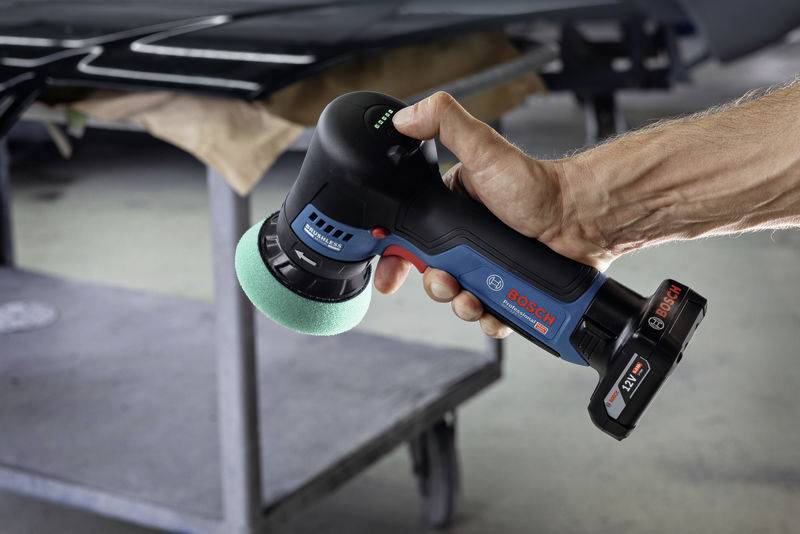 Egy személy egy Bosch csiszológépet tart egy zöld polírozókoronggal, felkészülve egy felület megmunkálására.