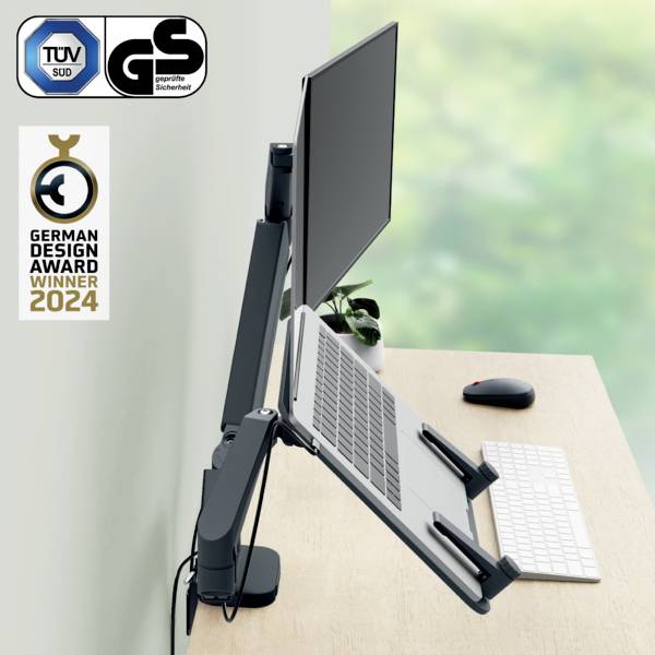 Egy laptop függőleges tartóban, monitorhoz csatlakoztatva, egy íróasztalon billentyűzettel. 'German Design Award Győztes 2024'.