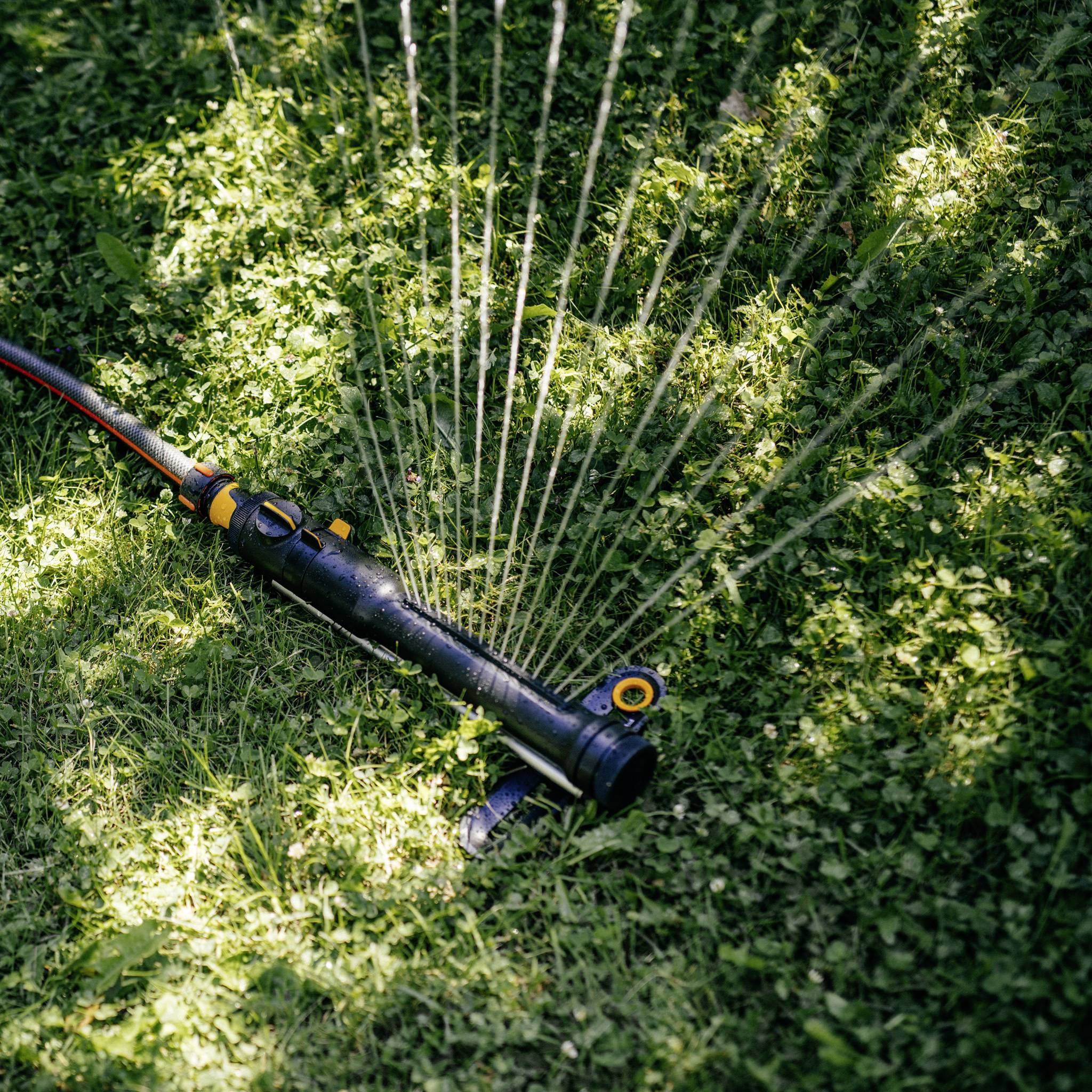 Egy kerti öntözőfej öntözi a zöld gyepet nappali fényben, a koncentrikus vízsugarai jól láthatóak a füvön.