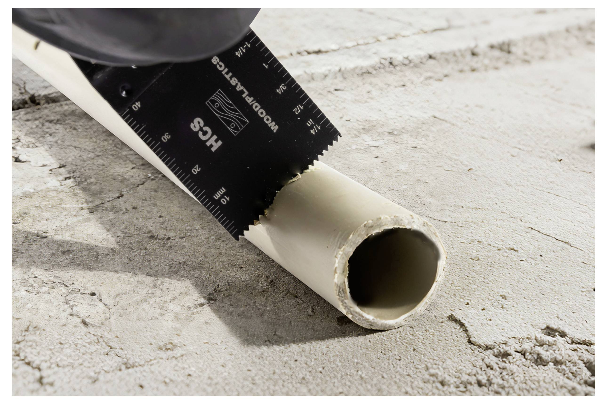 A fűrészlap egy műanyag csövet vág át egy betonfelületen, miközben tiszta metszést hoz létre.