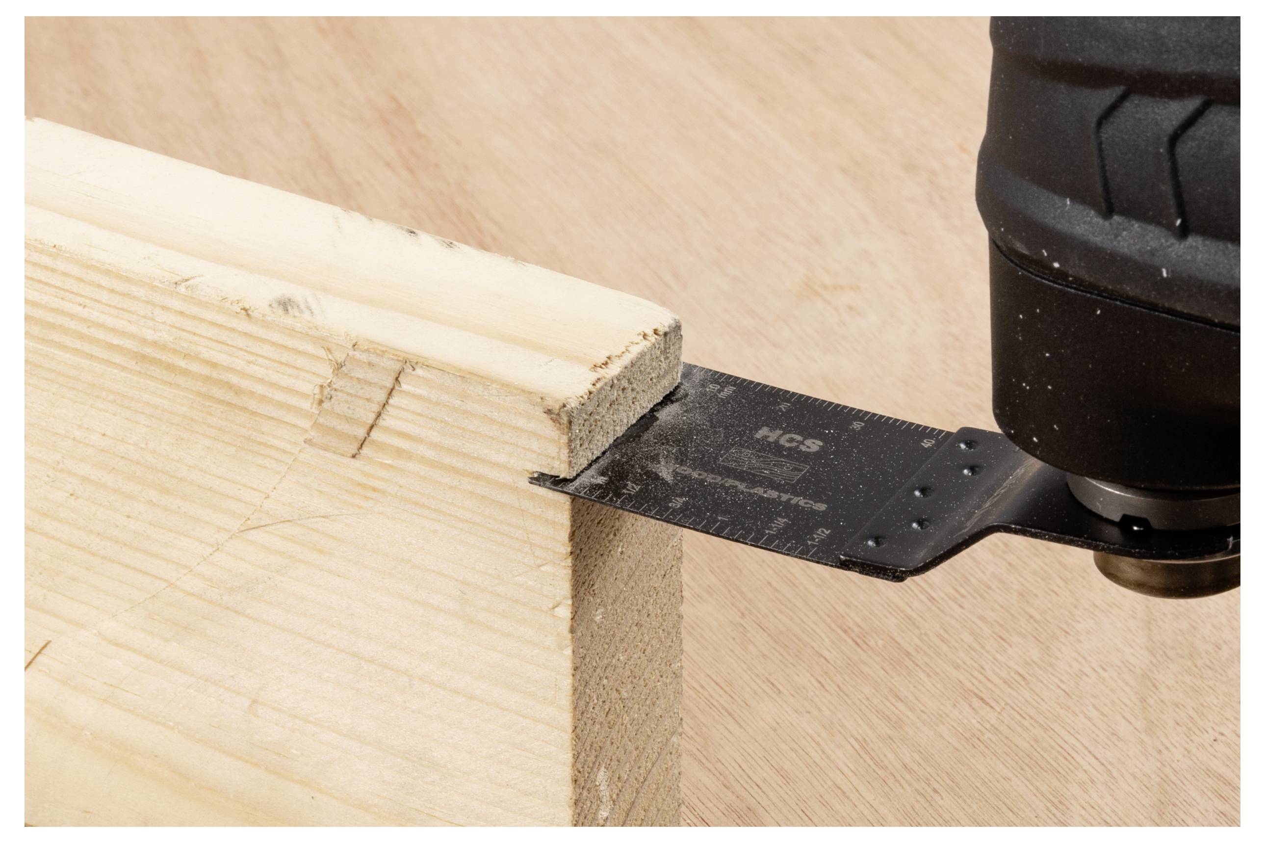 Egy fekete pengéjű erőgép egy világos színű fadarabot vág egy sima felületen.