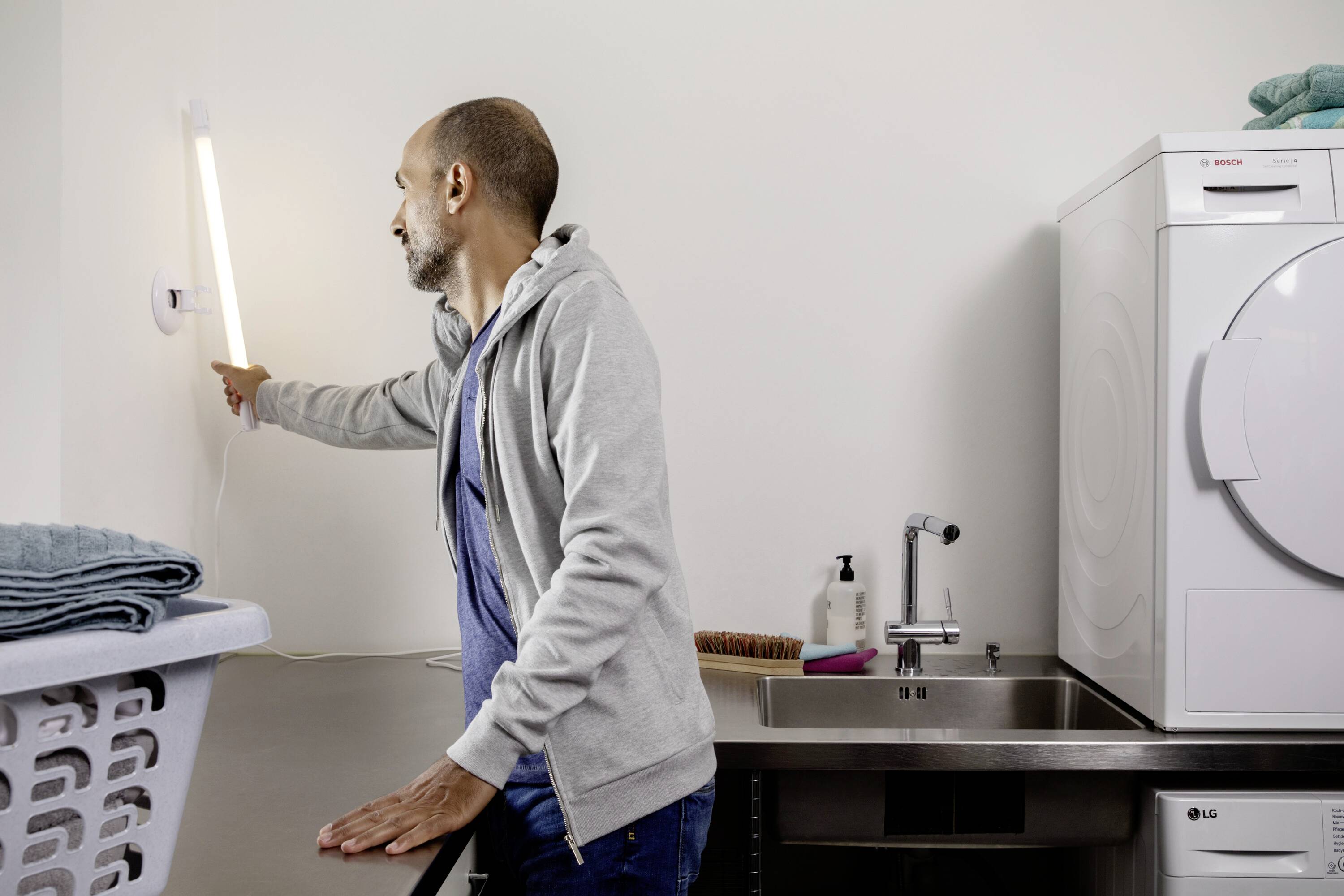 Egy férfi bekapcsolja a villanyt egy háztartási helyiségben. Egy mosógép és egy szárítógép mellett áll.