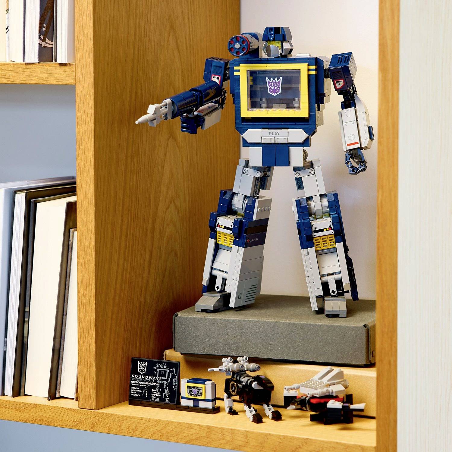 Egy modell robot áll egy polcon könyvek és kisebb játékok társaságában.