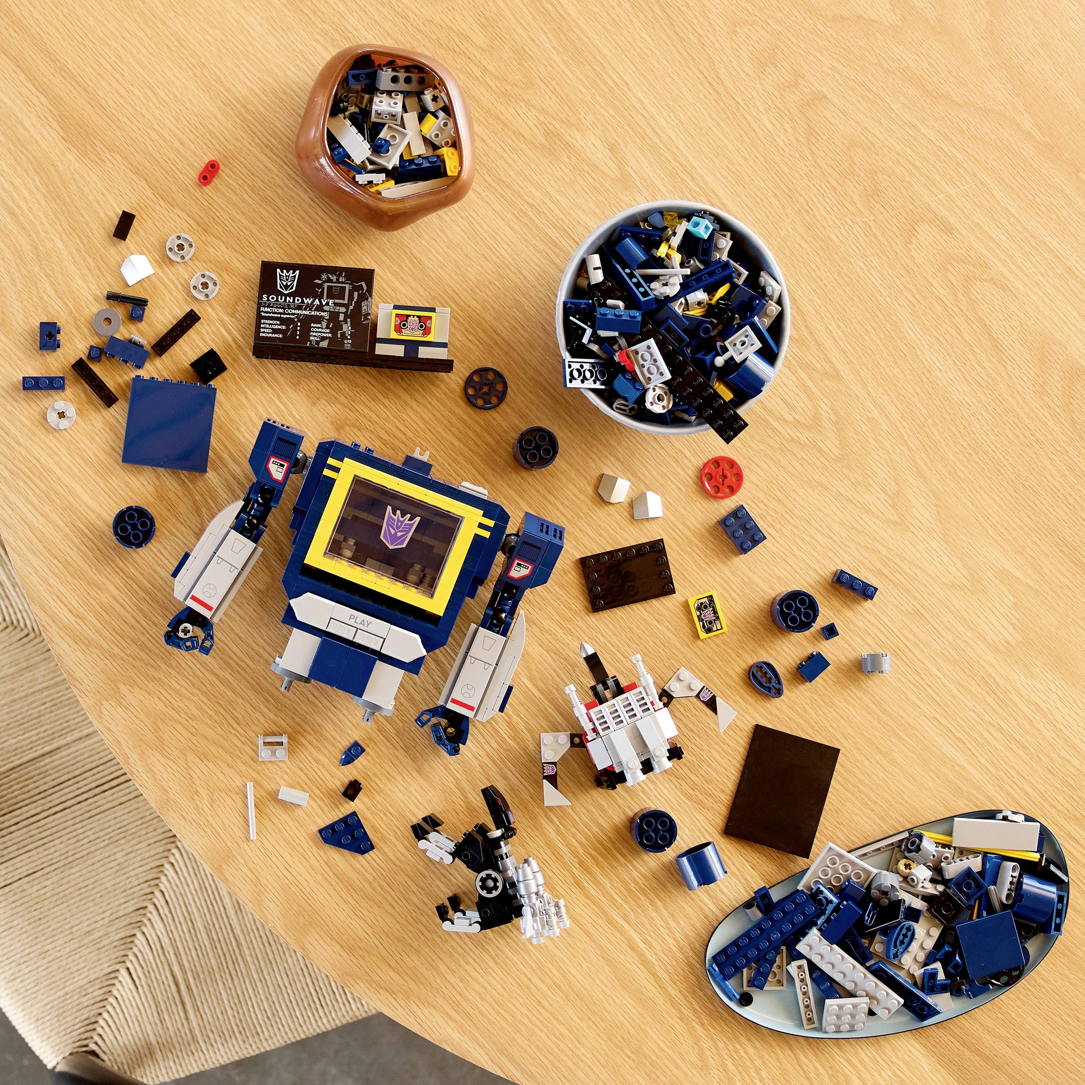 Különböző LEGO darabok és részben összeszerelt modellek vannak szétterítve egy kerek fa asztalon, köztük egy robot és vegyes építőelemek.