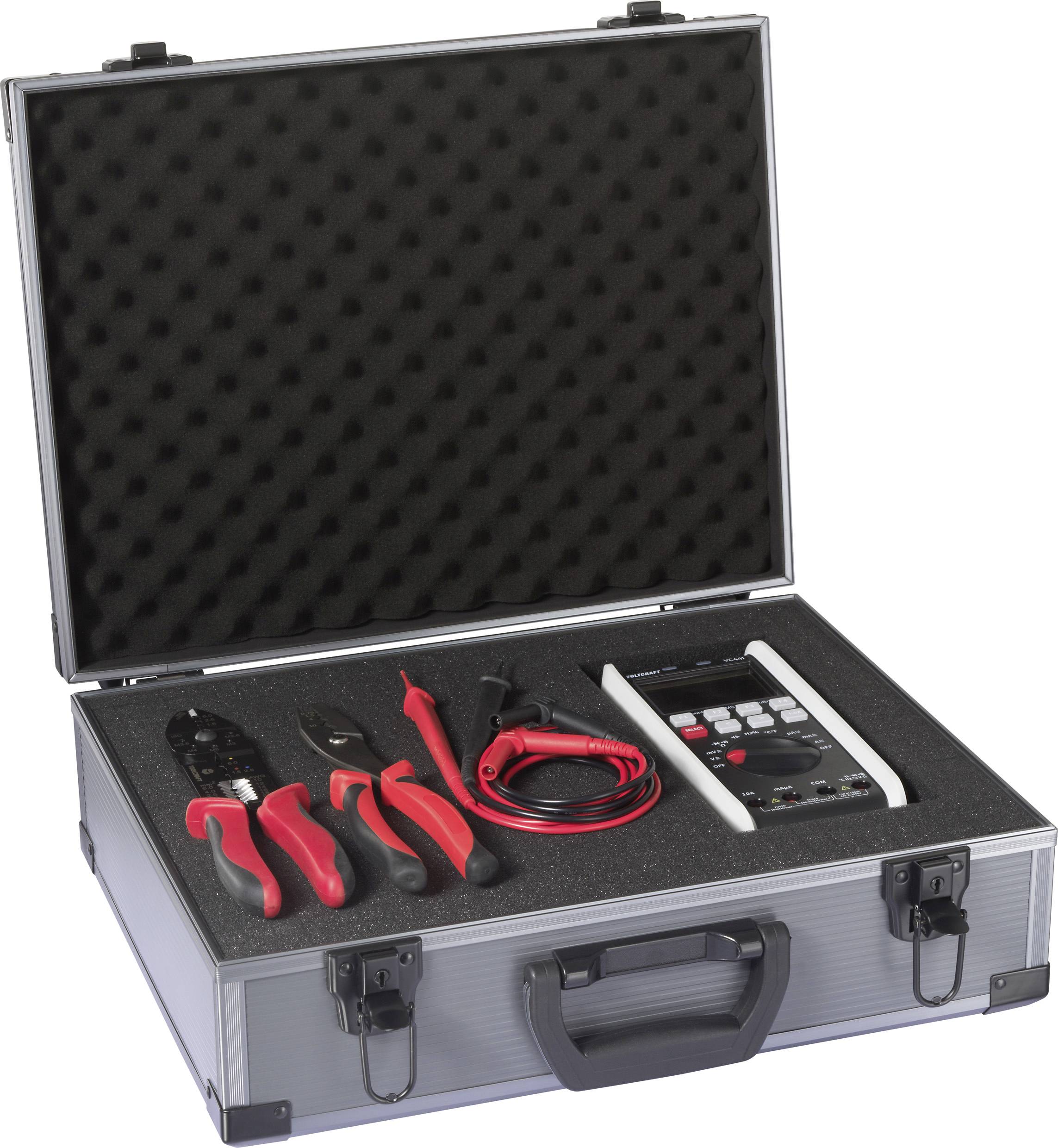 Egy nyitott ezüst tok vörös markolatú fogókkal, kábelcsípővel, kábel-készlettel és egy fekete habszivacs béléssel ellátott elektronikus multiméterrel.