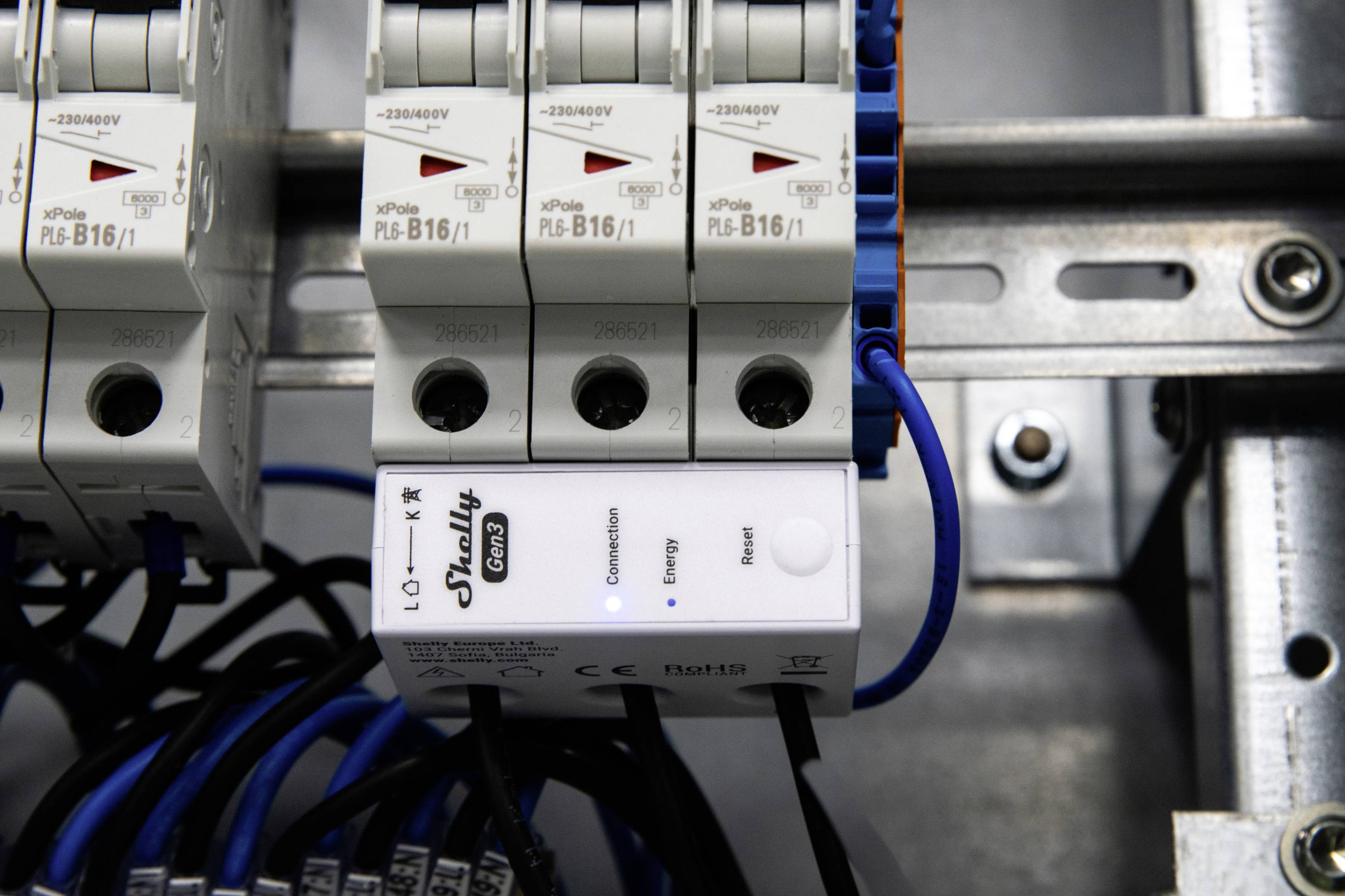 Egy közelkép elektromos kismegszakítókról, amelyek egy fémkeretbe vannak szerelve, és láthatóak a különböző kapcsolók, valamint az alján lévő bekötött kábelek.
