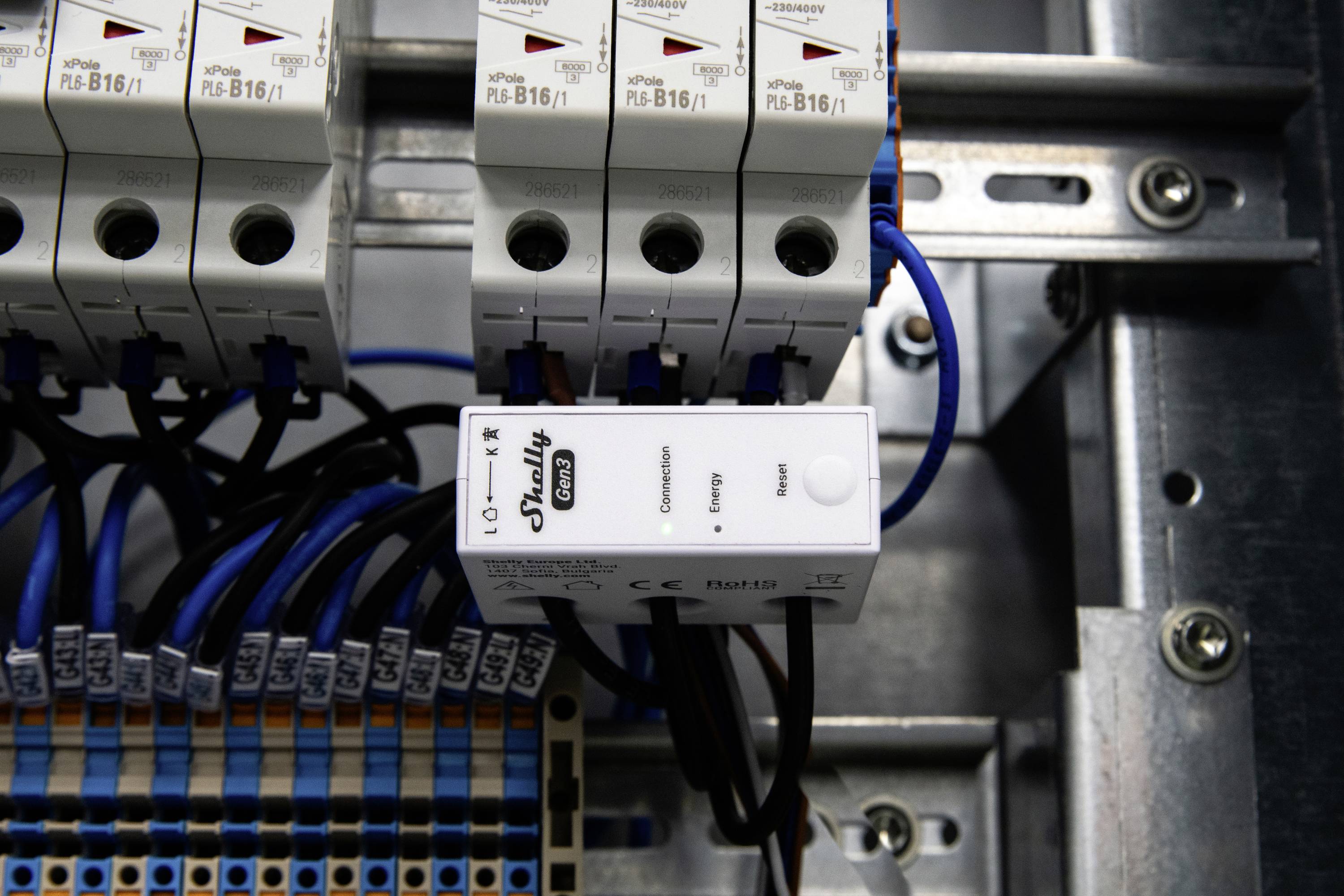 Egy elektromos elosztótábla áramköri megszakítókkal és egy Shelly 1 relével, amely automatizálási célokat szolgál. A kábelek rendezetten vannak csatlakoztatva, ami rendezett vezetékezésre utal.