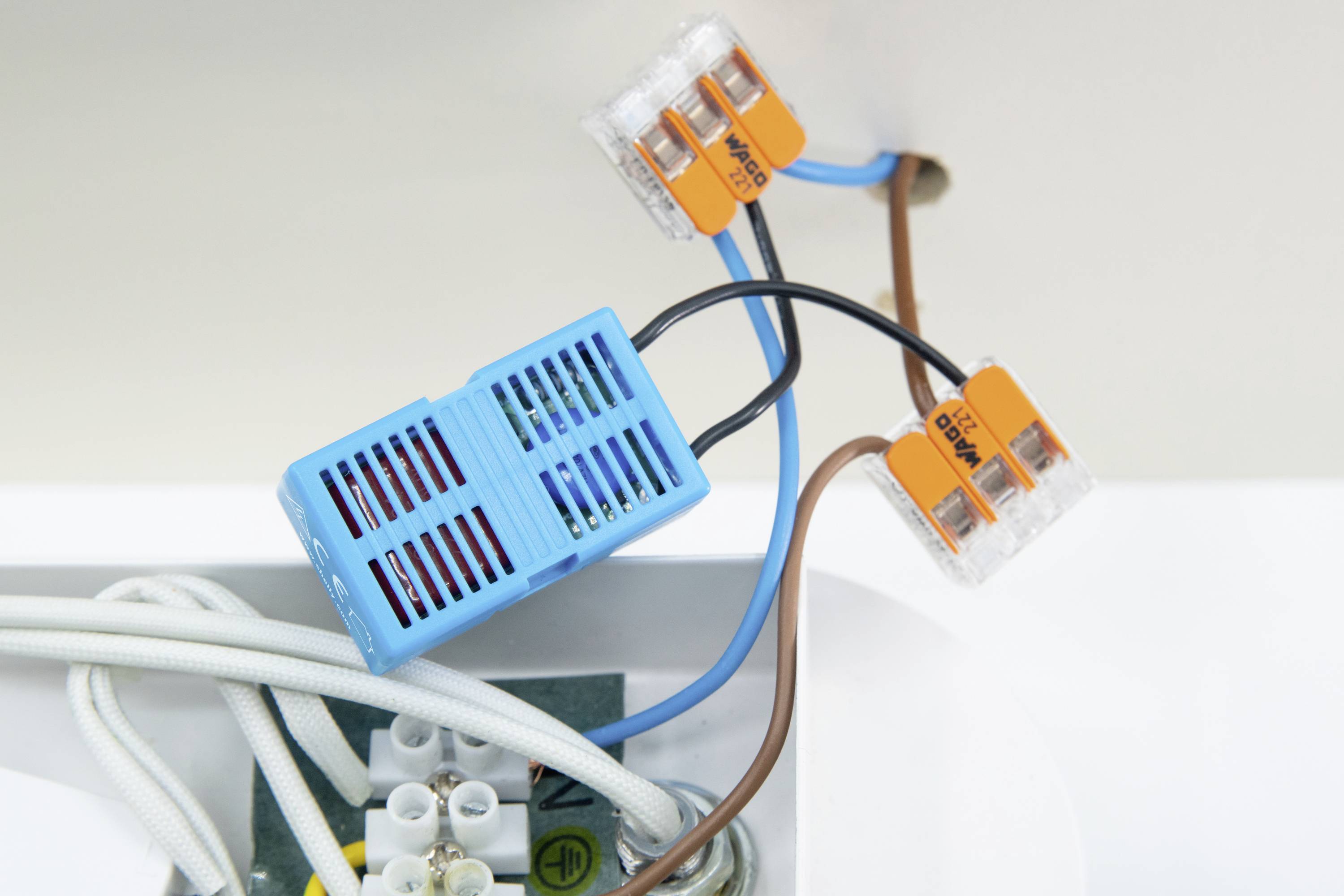 Egy kék elektronikai alkatrész narancssárga vezetékcsatlakozókkal fehér felületen, amely egy alapvető áramköri elrendezést mutat oktatási célból.