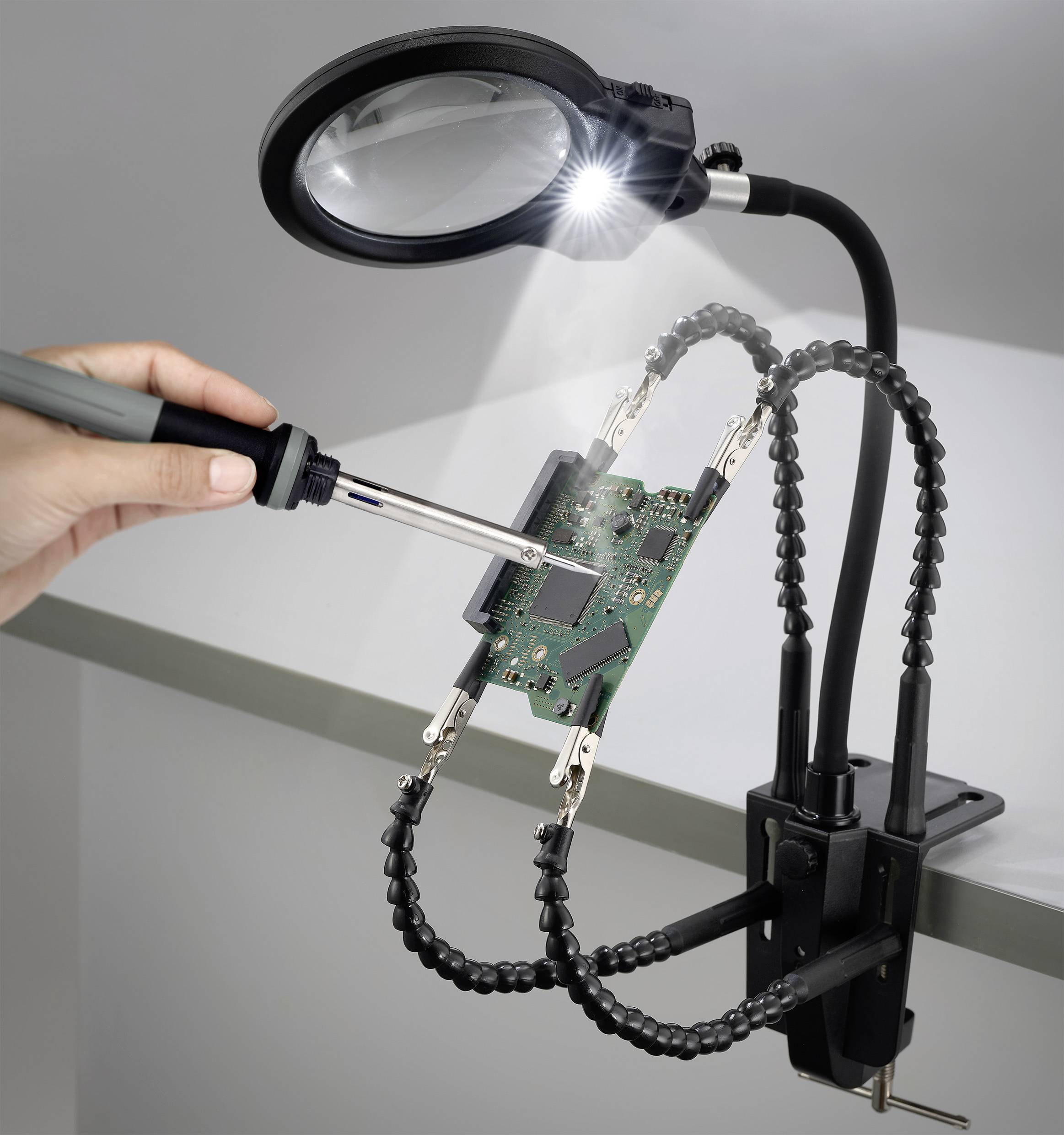 Egy ember egy áramköri lapot forraszt, amelyet egy rugalmas csiptetős állvány tart, hozzákapcsolt nagyítóval és lámpával, elektronikai munkát bemutatva.