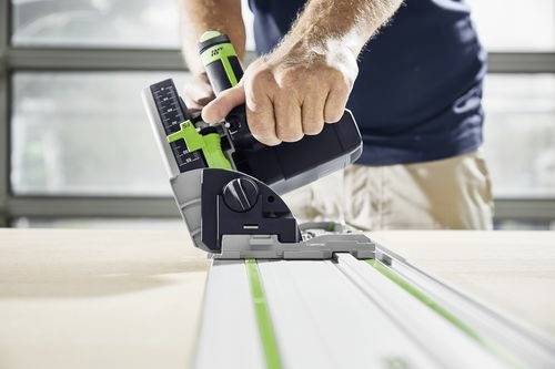 Egy személy egy körfűrészt kezel egy fa felületen, miközben precíziós vágásra összpontosít egy zöld vezetősáv mentén egy műhelyszerű környezetben.