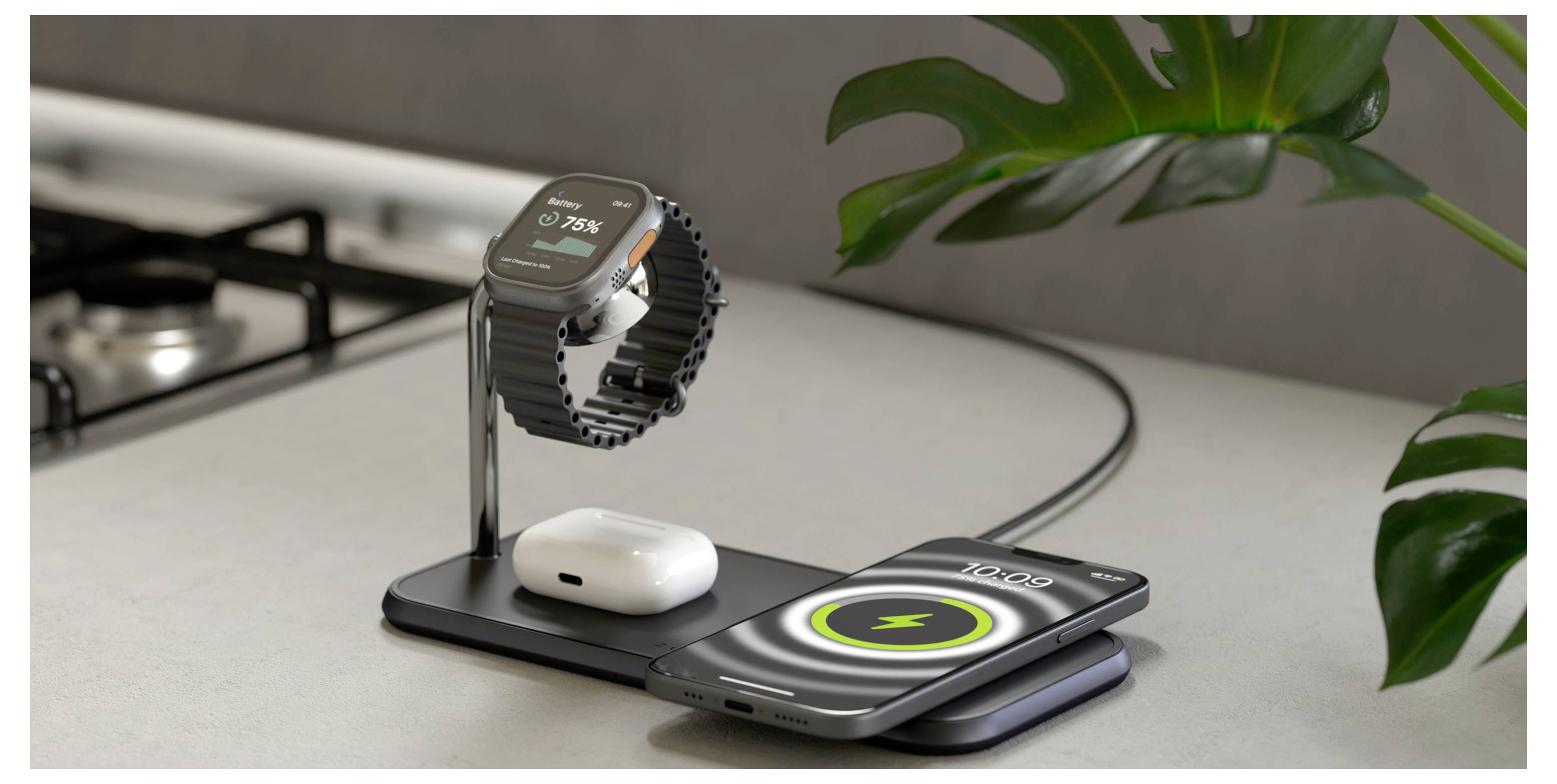 Egy okosóra, vezeték nélküli fülhallgató és okostelefon töltődik egy elegáns, modern töltőállomáson a konyhapulton, egy zöld növény közelében.