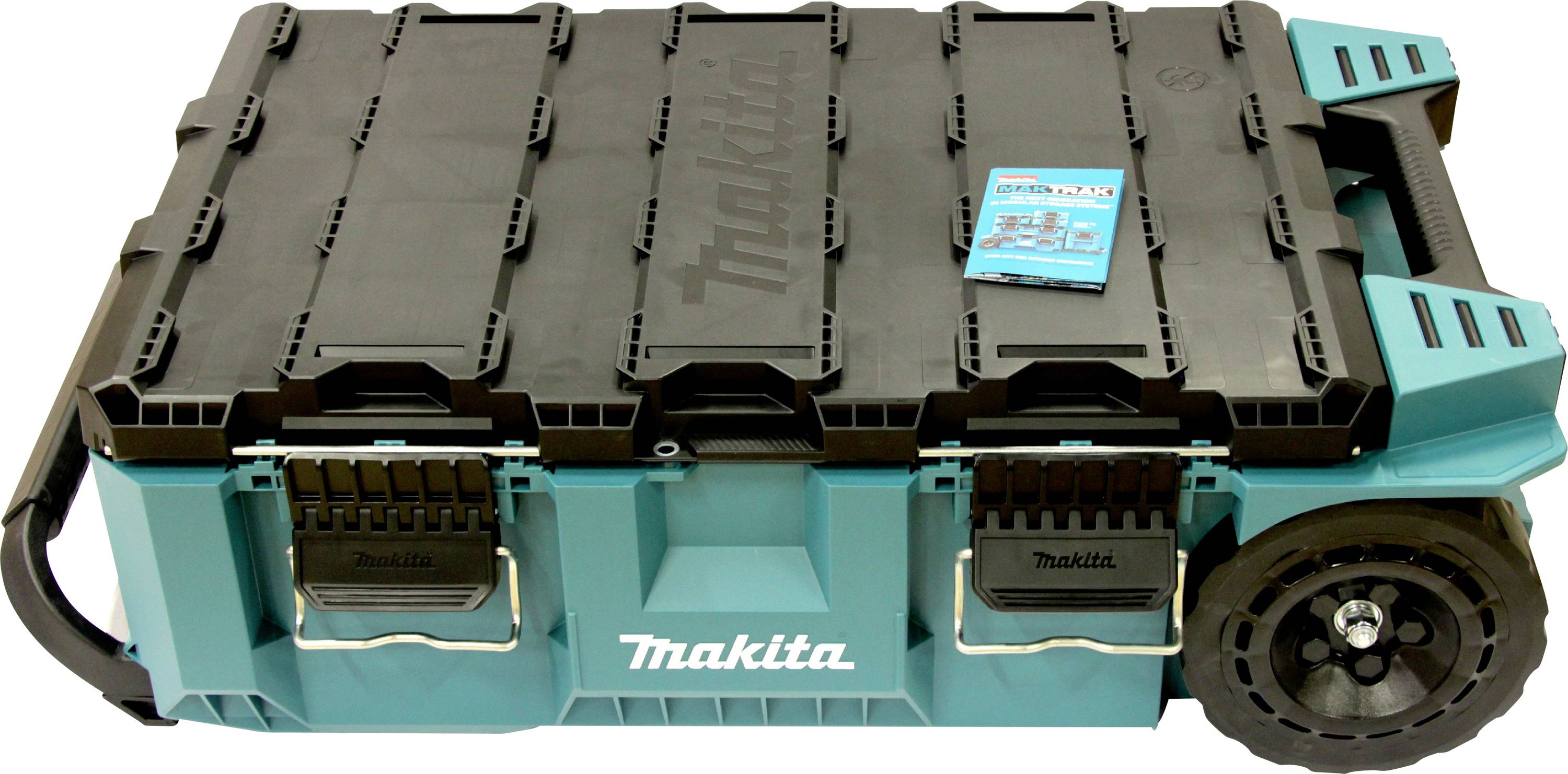 Fekete tetejű 'Makita' szerszámtároló doboz, két első retesszel, jobb oldalán kerekekkel és fogantyúval. Tetején egy kisméretű kék kézikönyv található.