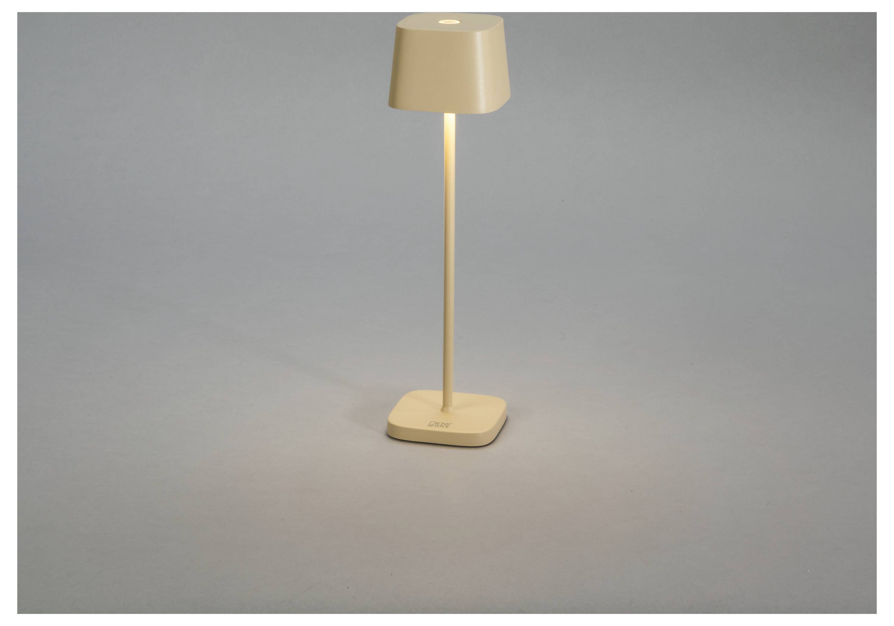 Egy bézs asztali lámpa világít, egy sima felületen áll, meleg fényt árasztva.