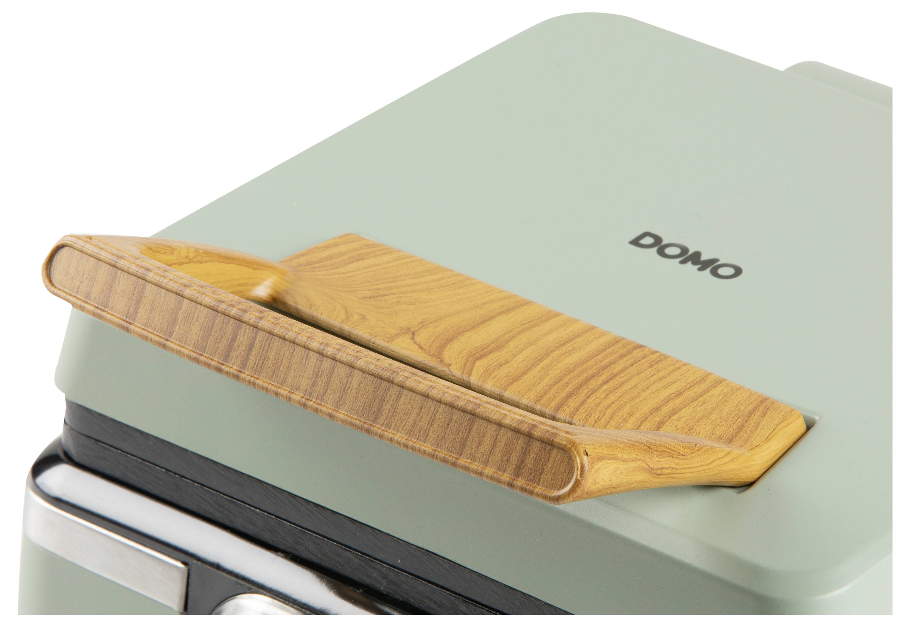Egy közeli felvétel egy zöld háztartási eszközről, fa fogantyúval, amelyen a 'DOMO' márkanév látható, kiemelve a fogantyú formatervezését és a márkajelzést.