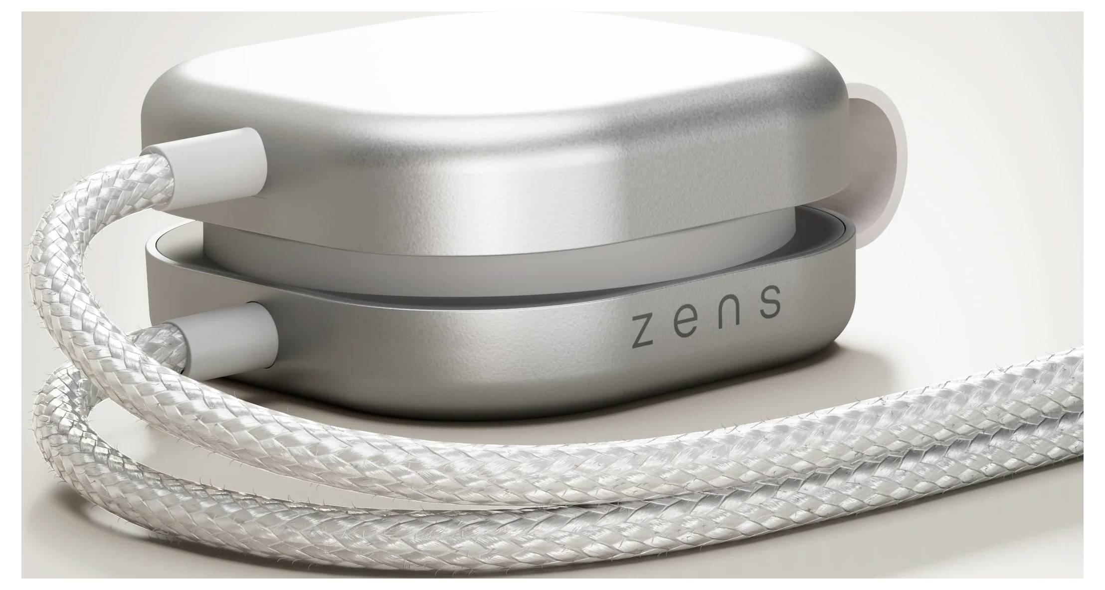 Egy kompakt vezeték nélküli töltő, elegáns kerek formatervezéssel, fémes felülettel és fonott kábellel, amelynek az oldalán 'zens' felirat látható.