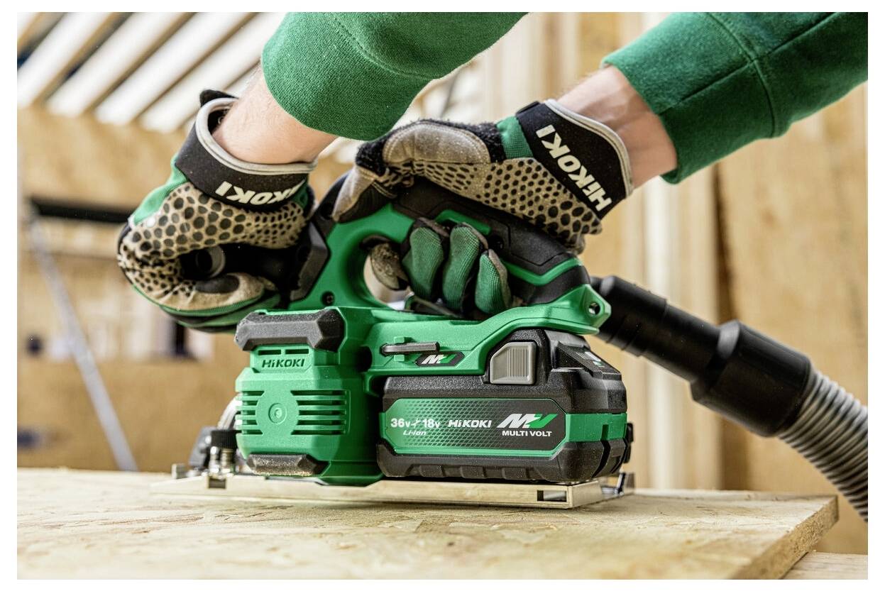 Egy személy egy zöld és fekete kéziszerszámot használ fa csiszolásához, védőkesztyűt viselve. A szerszámon a "Hikoki 36V 18V MultiVolt" felirat látható.
