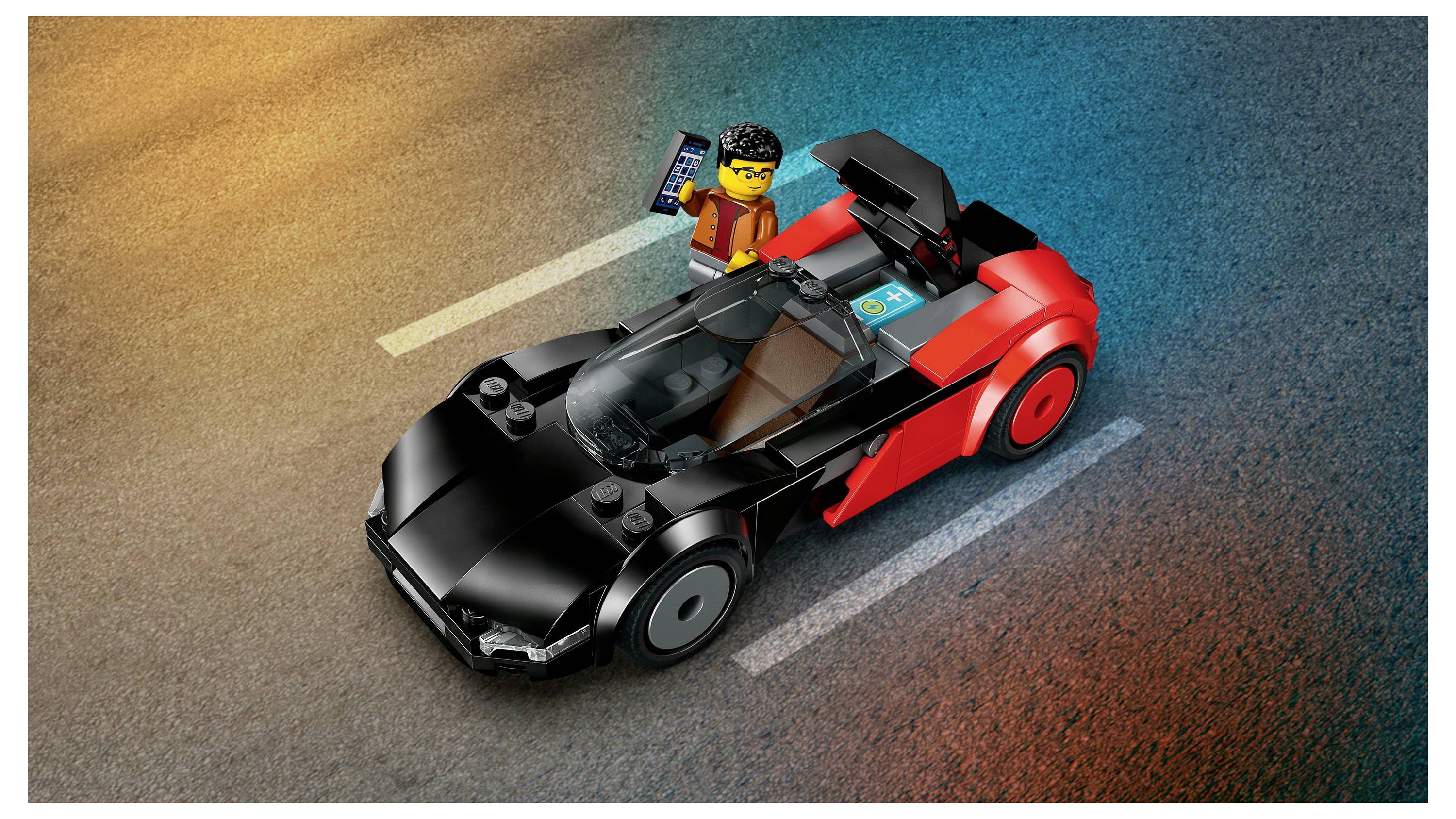 Egy LEGO figura áll egy úton egy fekete és piros LEGO sportautó mellett, kezében egy táblagéppel.