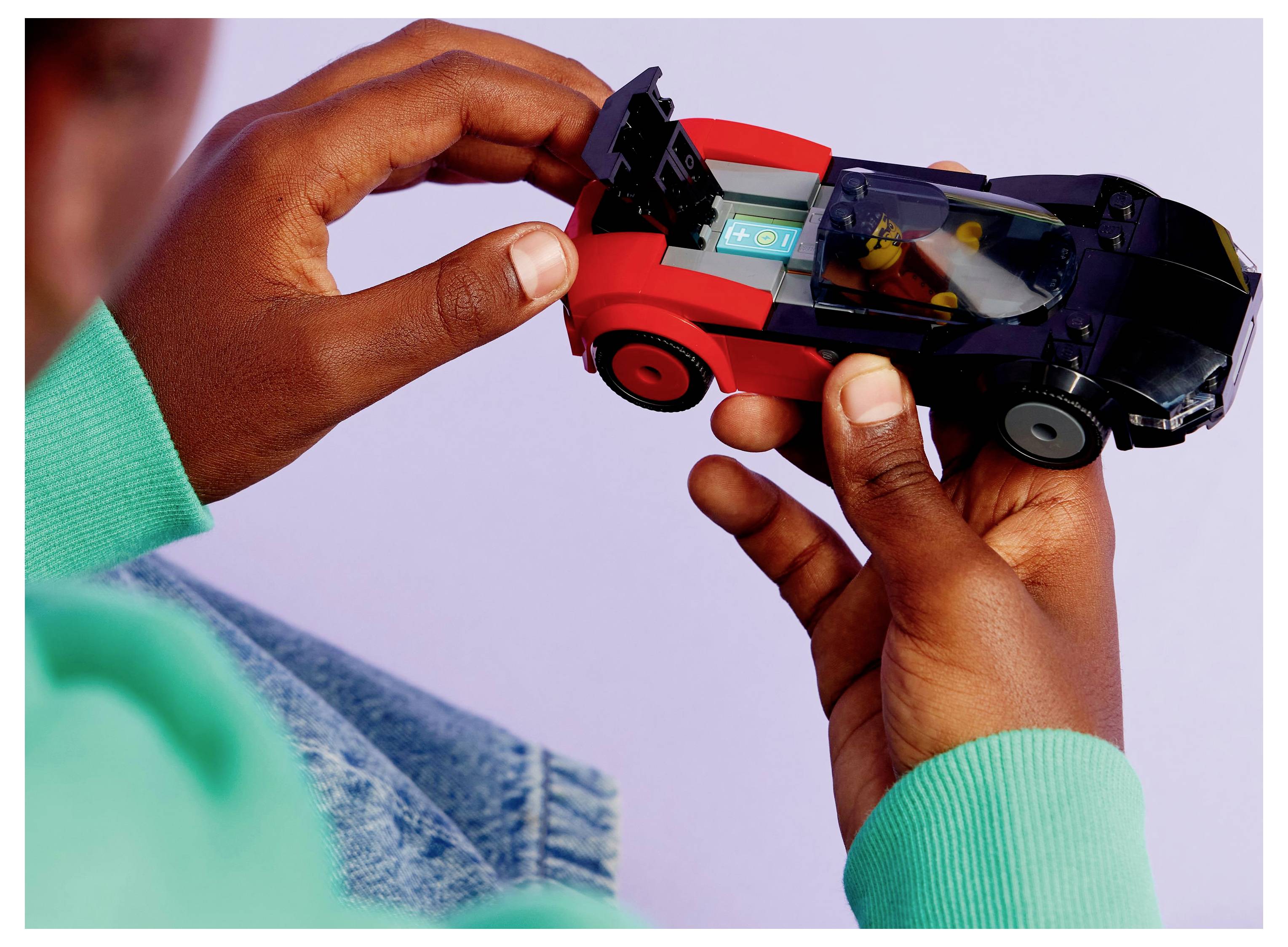 Egy kisgyermek egy kis piros és fekete játékautóval játszik, a részletekre összpontosítva, egy minifigura ül bent, lágy háttér előtt.