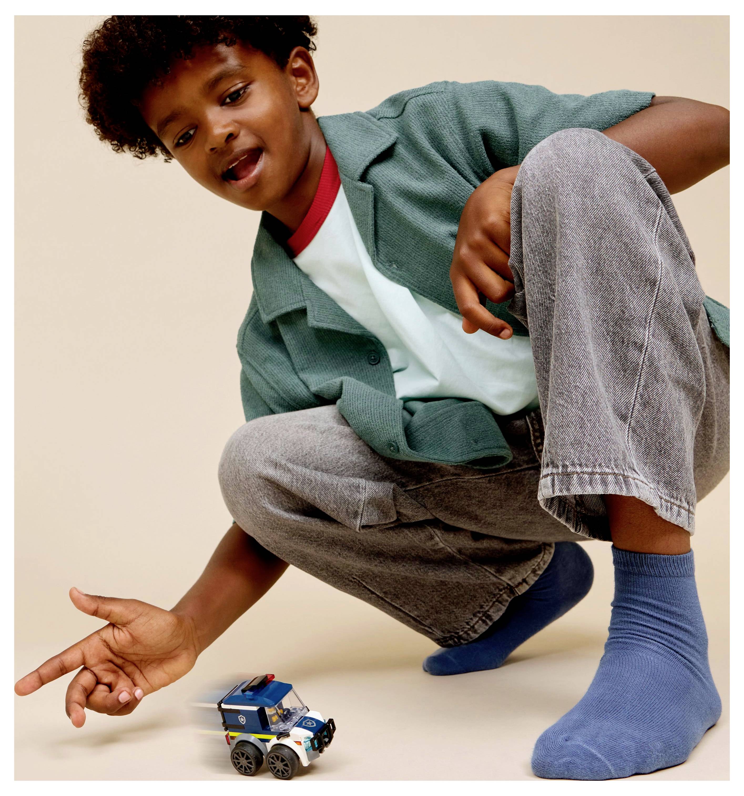 Egy gyerek guggol a padlón, és egy kis játék rendőrautóval játszik világos háttér előtt.