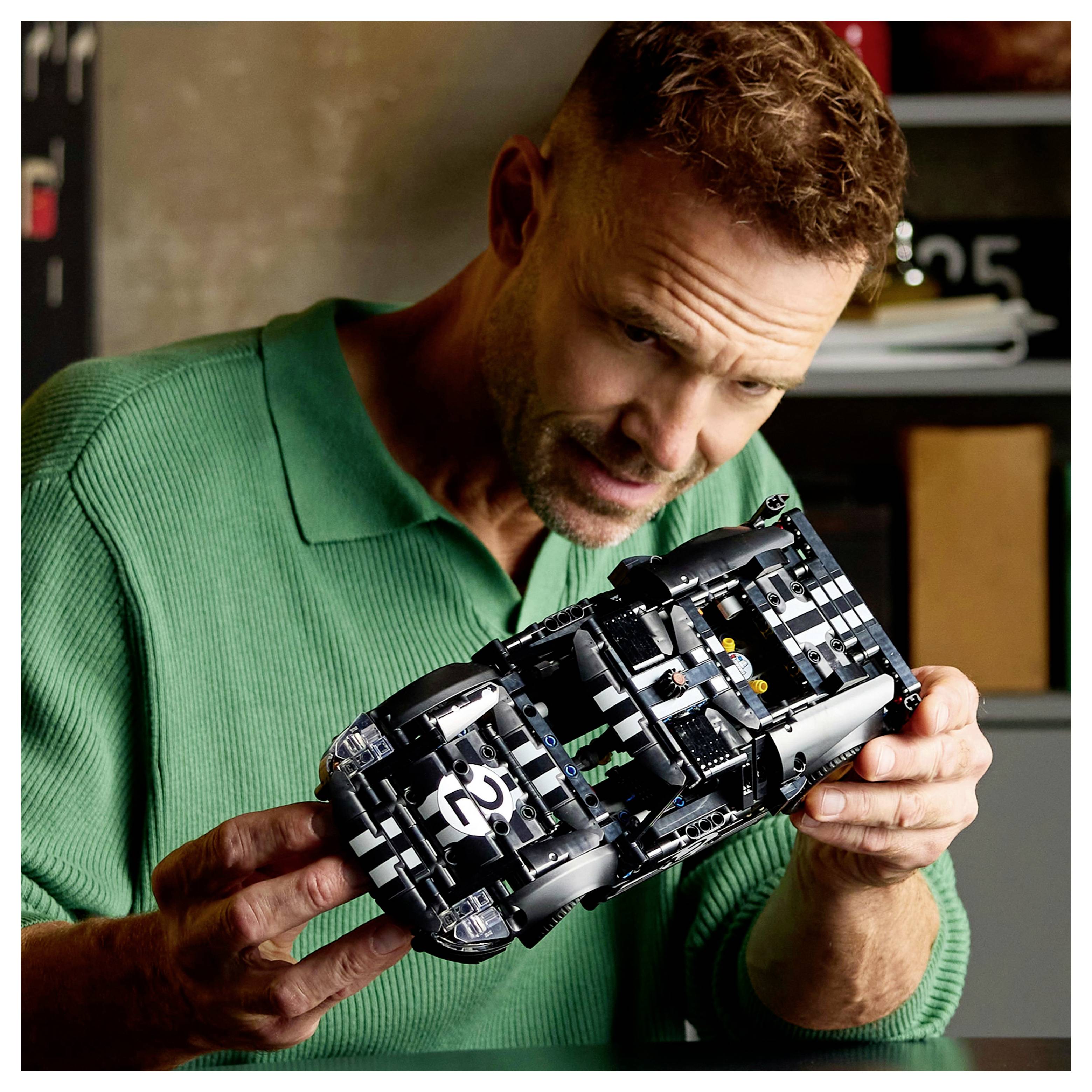 Egy zöld pulóvert viselő férfi egy fekete, 25-ös számú modellautót vizsgál egy garázsszerű környezetben.