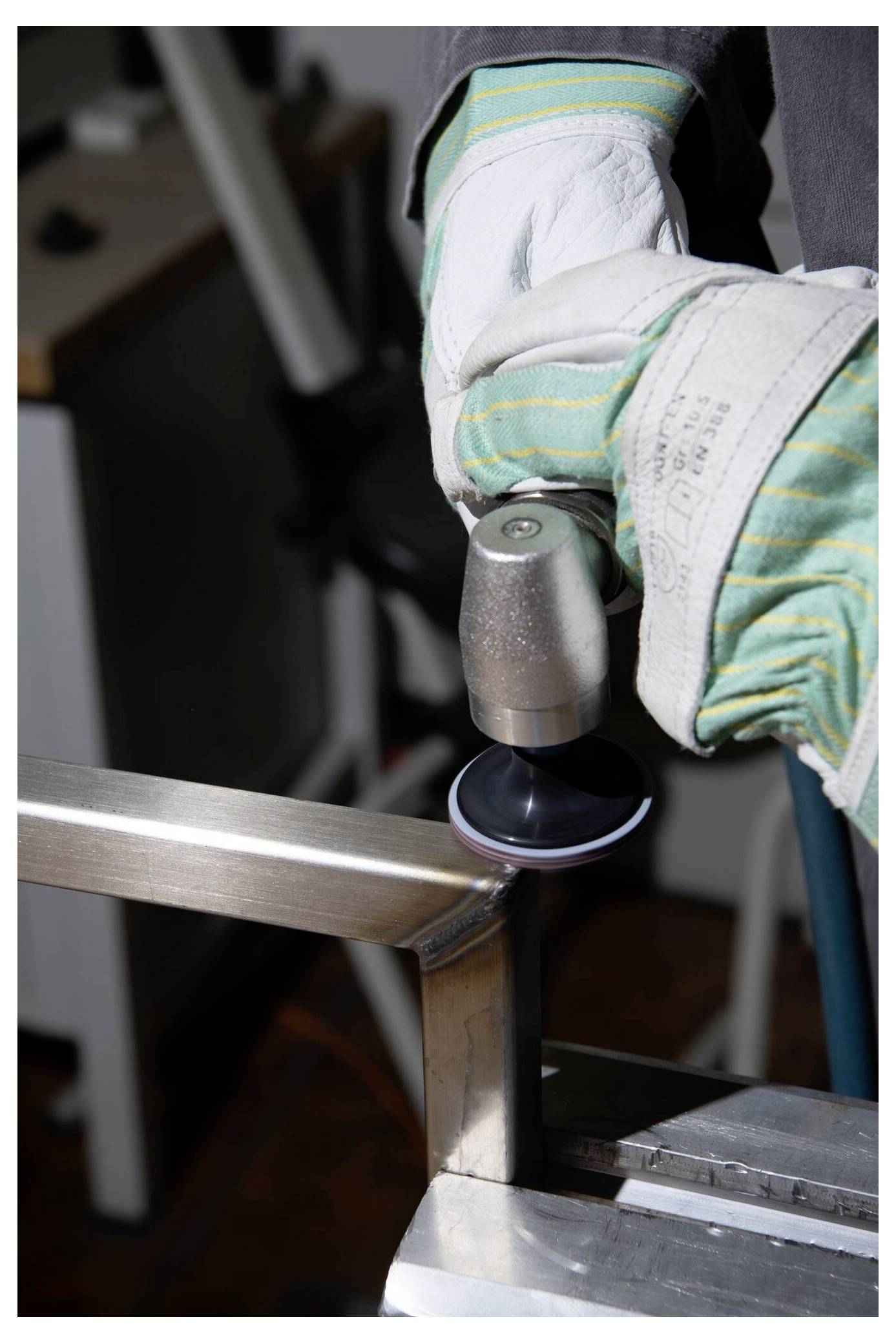 Kesztyűs kezek egy erőgépet használnak egy fémkeret sarkának polírozásához.