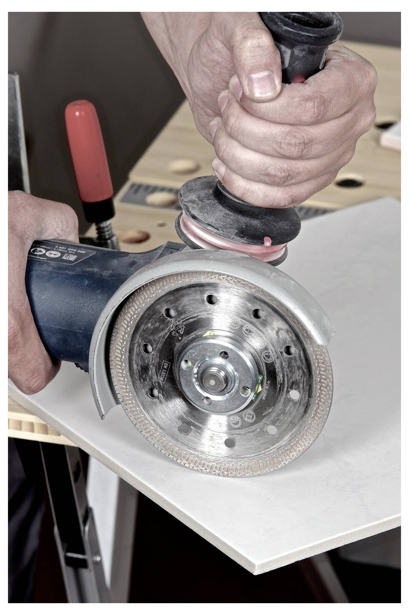 Egy személy egy sarokcsiszolóval vág egy csempét egy munkapadon, ezzel egy otthoni felújítási vagy építkezési tevékenységet mutatva be.