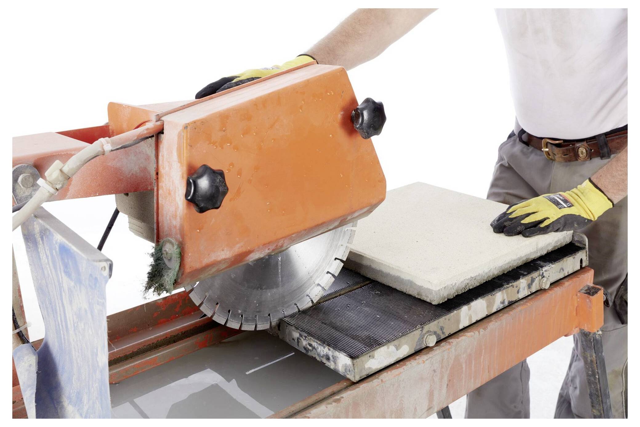 Egy védőkesztyűt viselő személy egy asztali körfűrésszel vág egy téglalapú betonlapot. A fűrésznek nagy, köralakú pengéje van.