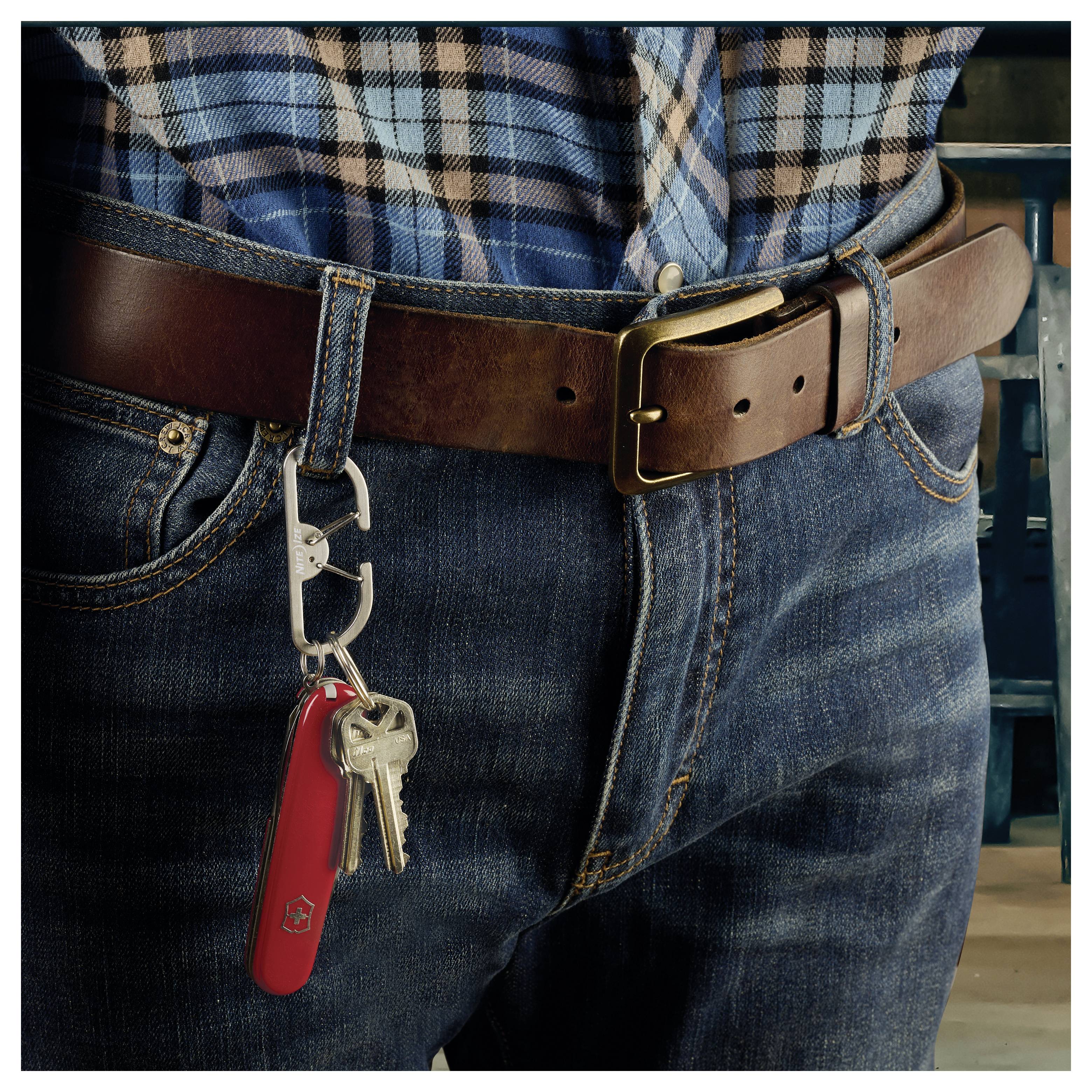 Egy ember farmert és kockás inget visel, bőrövvel, amelyre kulcsok és egy piros zsebkés van csatolva az övcsat mellé.