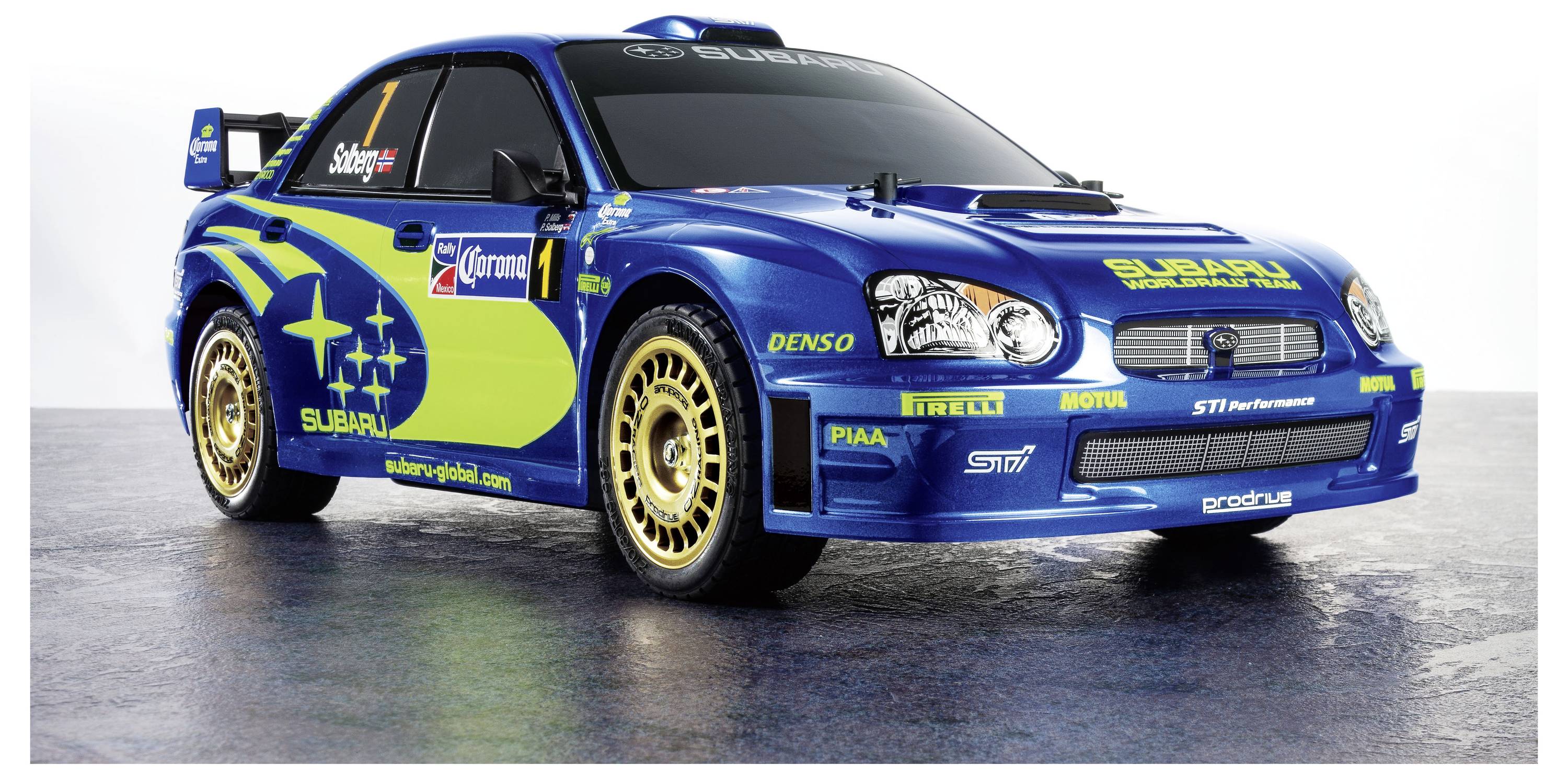 Egy kék és zöld Subaru rally autó, amelynek oldalán a 'Subaru' felirat és szponzori logók vannak, sportos dizájnnal és arany kerekekkel.