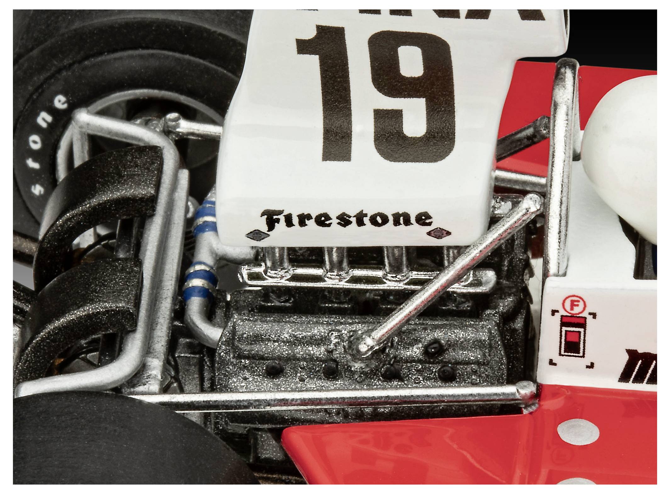 Egy veterán versenyautó közeli képe, amelyen egy fekete 'Firestone' logó látható a motor közelében, egy fehér uszonnyal, rajta egy nagy '19'-es szám, az autó teste pedig piros színű.