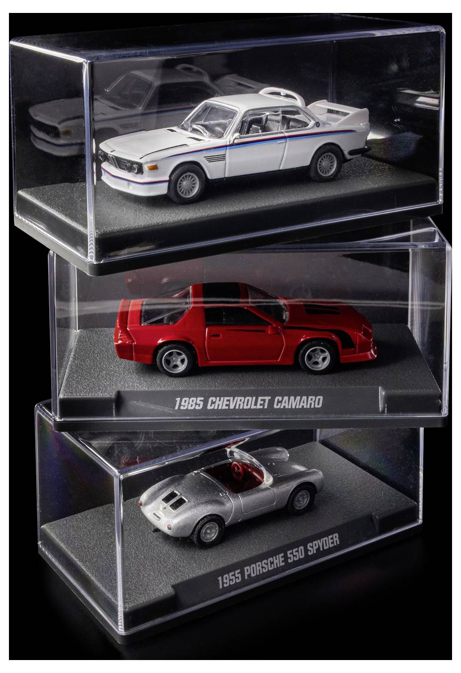 Három modellautó üvegvitrinben: egy fehér BMW, egy piros 1985-ös Chevrolet Camaro és egy ezüst 1955-ös Porsche 550 Spyder, függőlegesen egymásra helyezve.