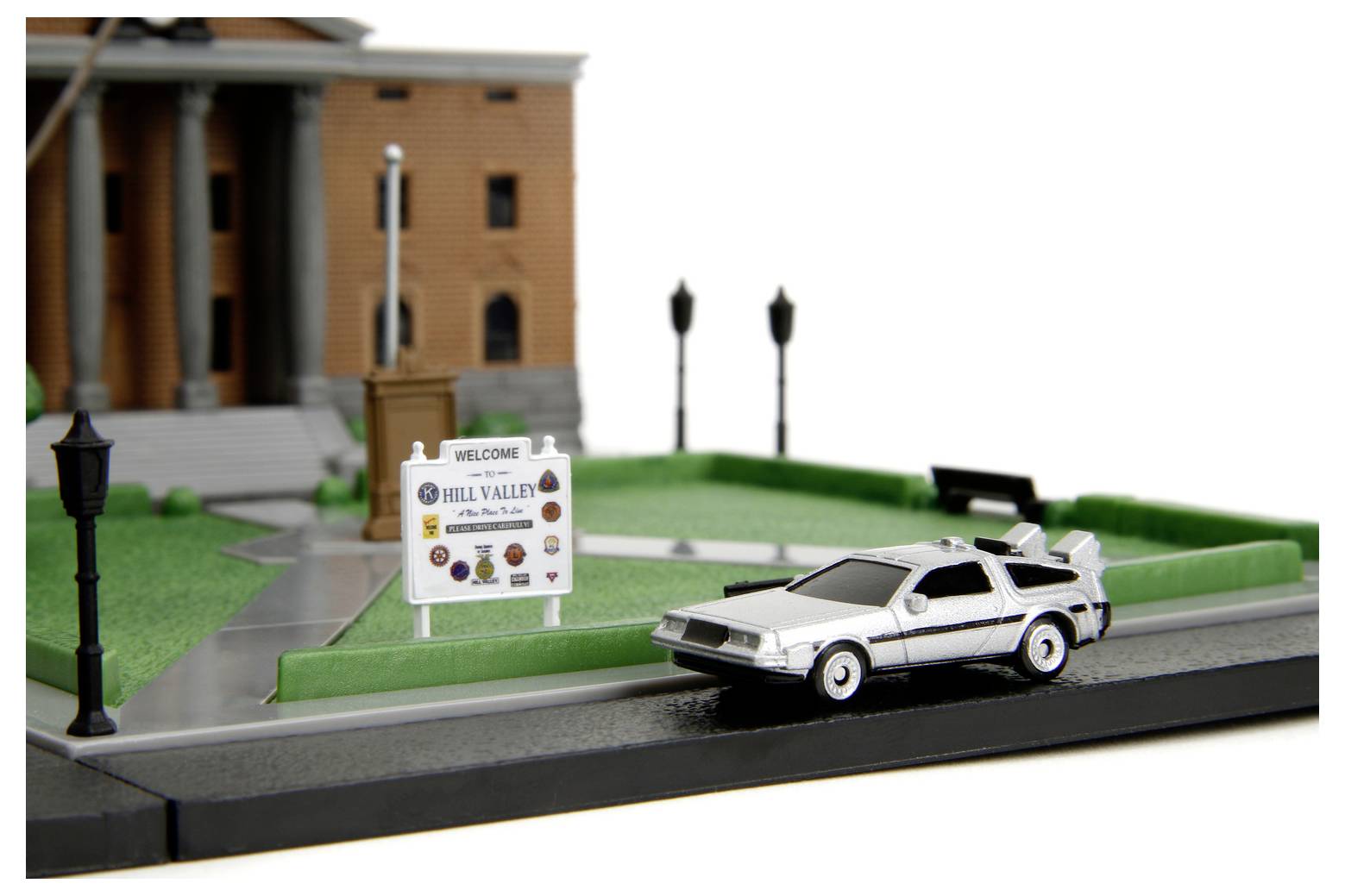 Egy kisméretű DeLorean autómodell egy miniatűr utcán áll egy 'Üdvözöljük Hill Valley-ben' tábla előtt, épülettel a háttérben.