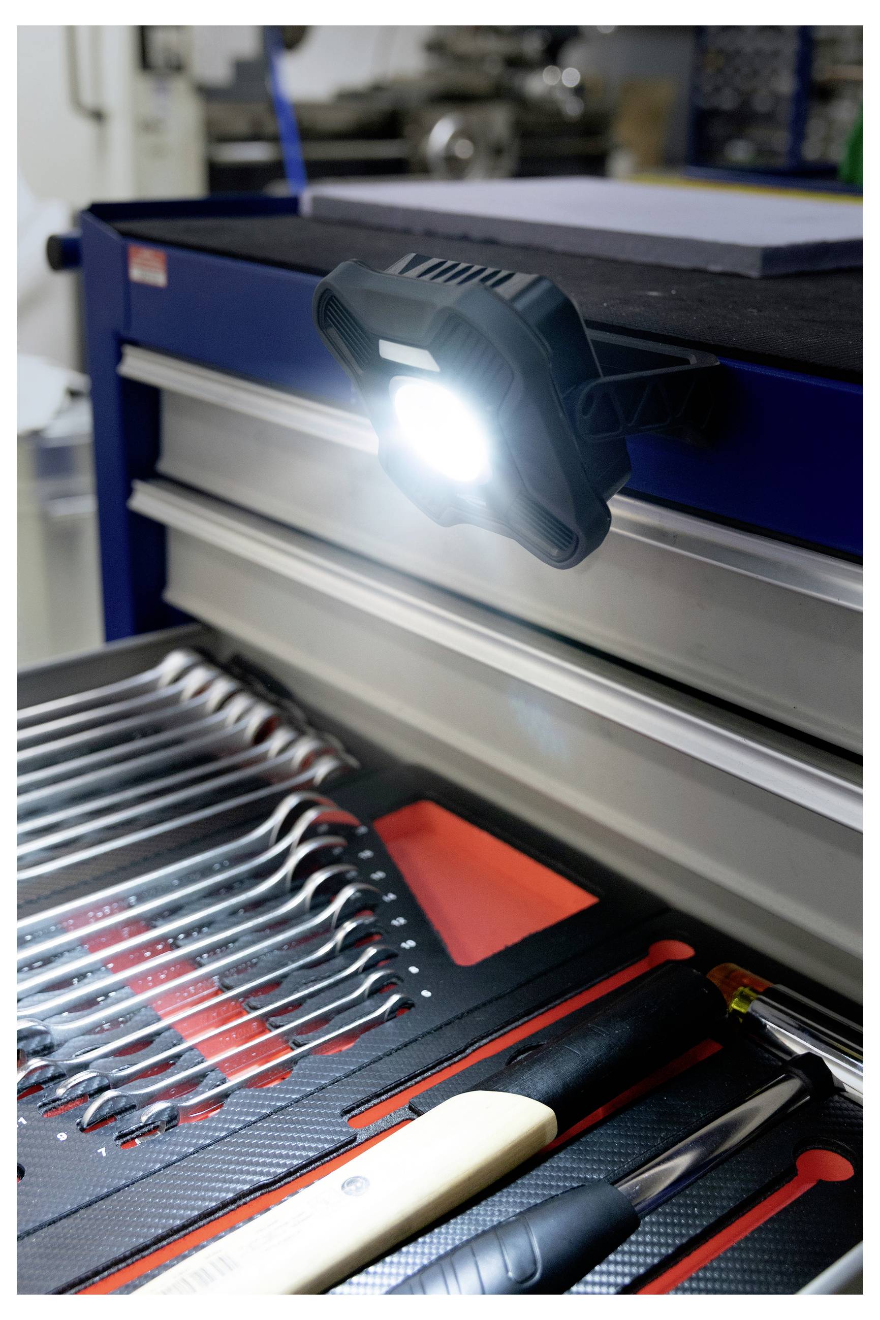 Egy égő szerelőlámpa egy kék szerszámosládára erősítve, amely megvilágítja a gondosan elrendezett csavarkulcsokat és szerszámokat egy műhelyi környezetben.