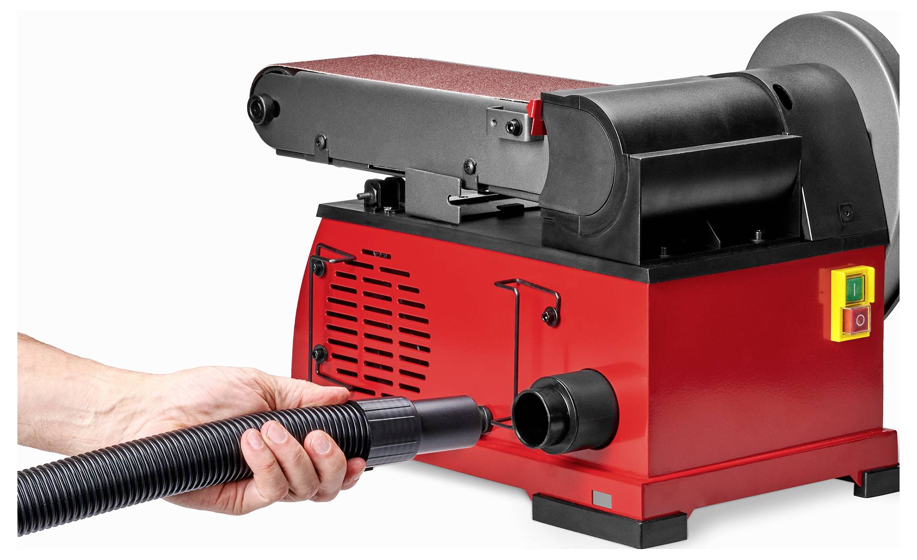 Egy személy egy tömlőt csatlakoztat egy piros szalagcsiszológéphez, amelynek por elszívó rendszere és látható bekapcsoló gombjai vannak az oldalán.