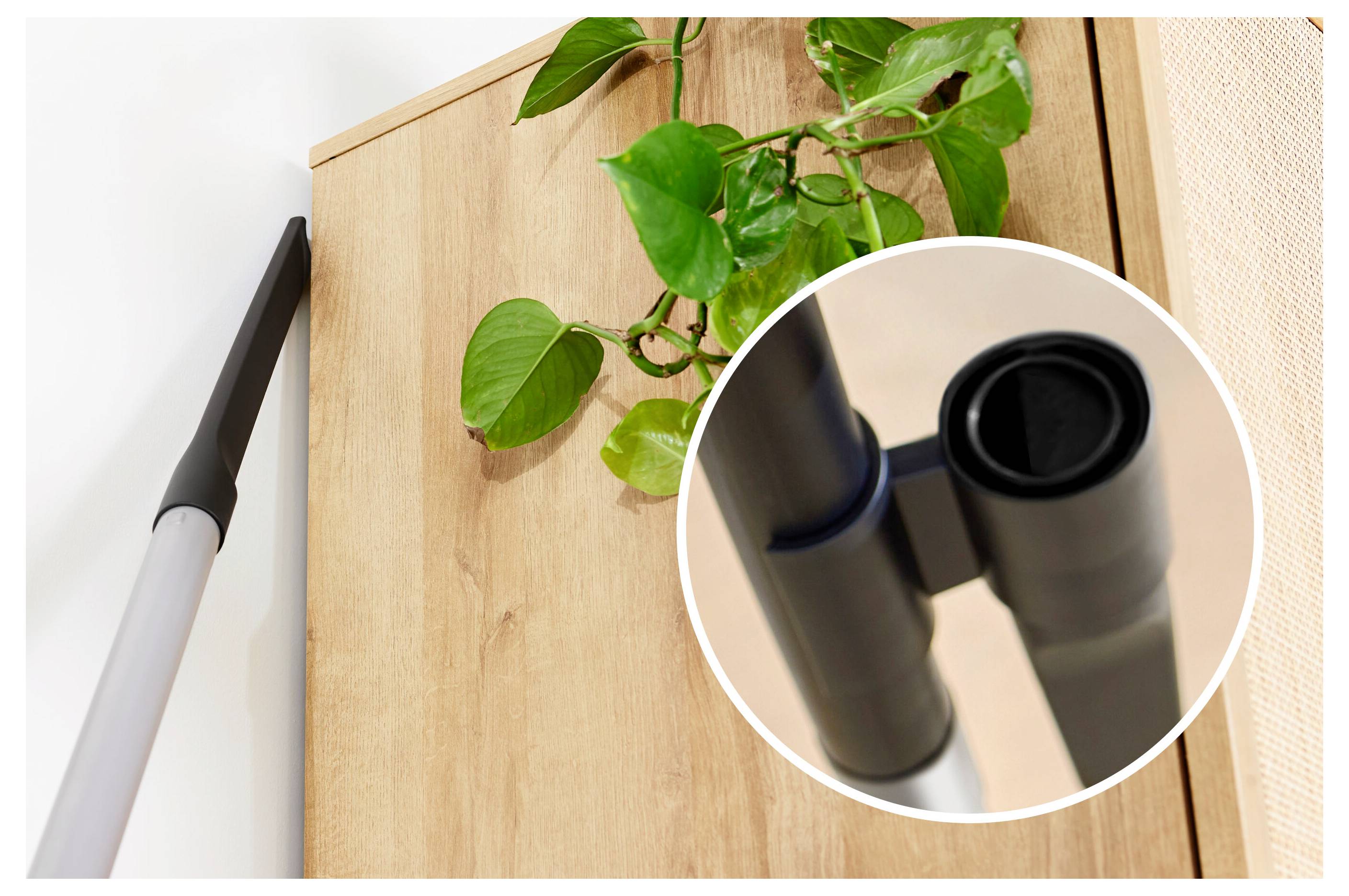 Egy porszívófej, amely egy magas szekrény sarkát éri el, egy betétképpel, amely a fúvóka hegyét mutatja. Egy növény van a szekrény tetején.