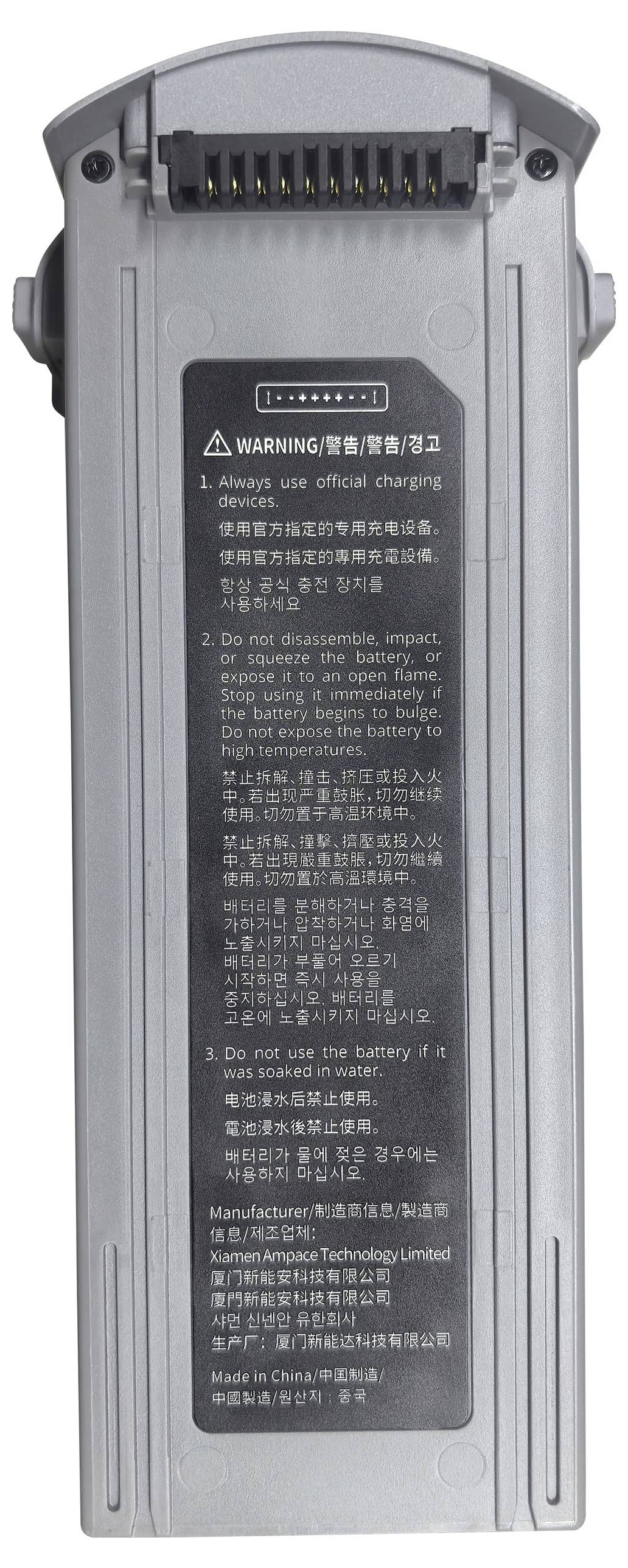 Egy szürke akkumulátor töltőcsatlakozókkal és több nyelven írt figyelmeztető címkékkel.