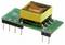 Egy kisméretű zöld áramköri lap, amelyre egy sárga téglalap alakú transzformátor van szerelve, fémcsatlakozókkal az összeköttetéshez.